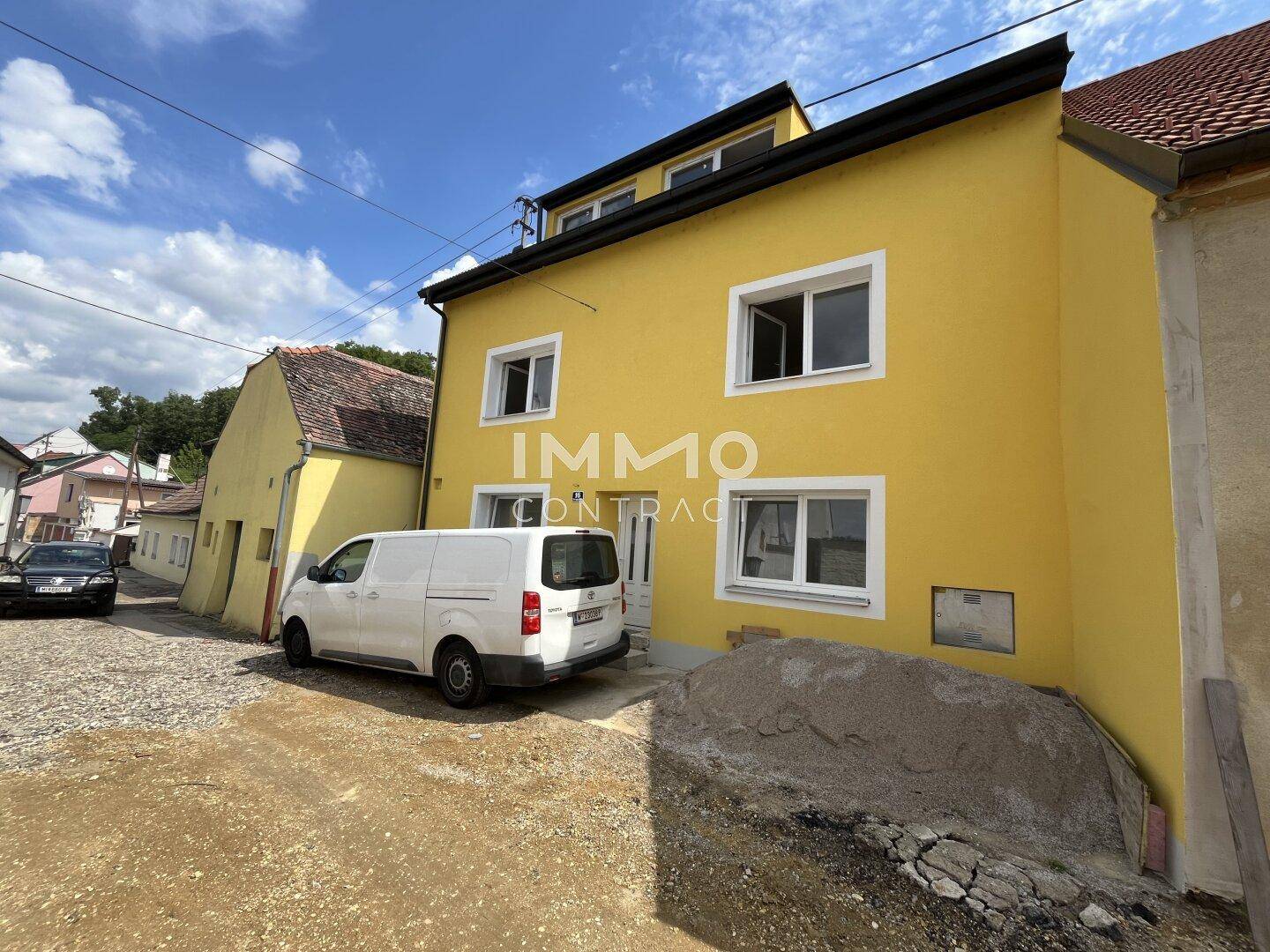 Gelbe Hausfassade mit weißen Fenstern und Eingangsbereich, umgeben von einer ländlichen Umgebung.
