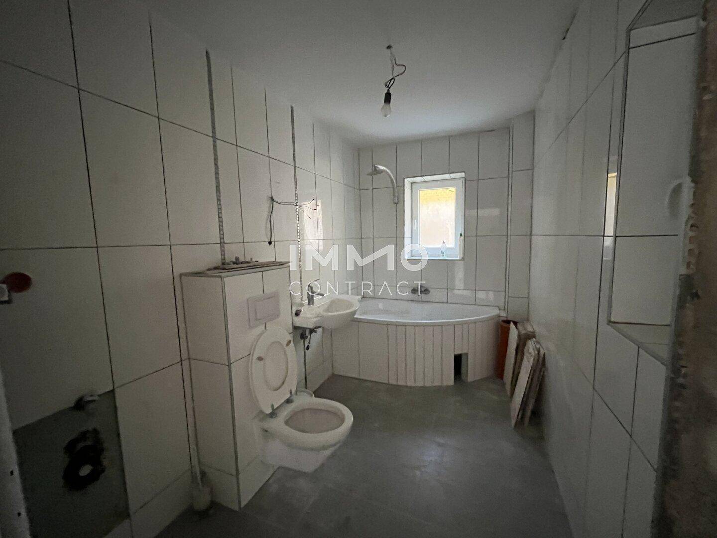 Badezimmer mit Eckbadewanne, Toilette und Fliesen an Wänden und Boden, bereit zur Fertigstellung.