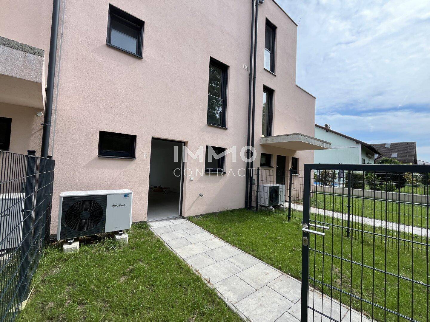 Hintereingang eines Reihenhauses mit Wärmepumpe und kleinem Gartenbereich.