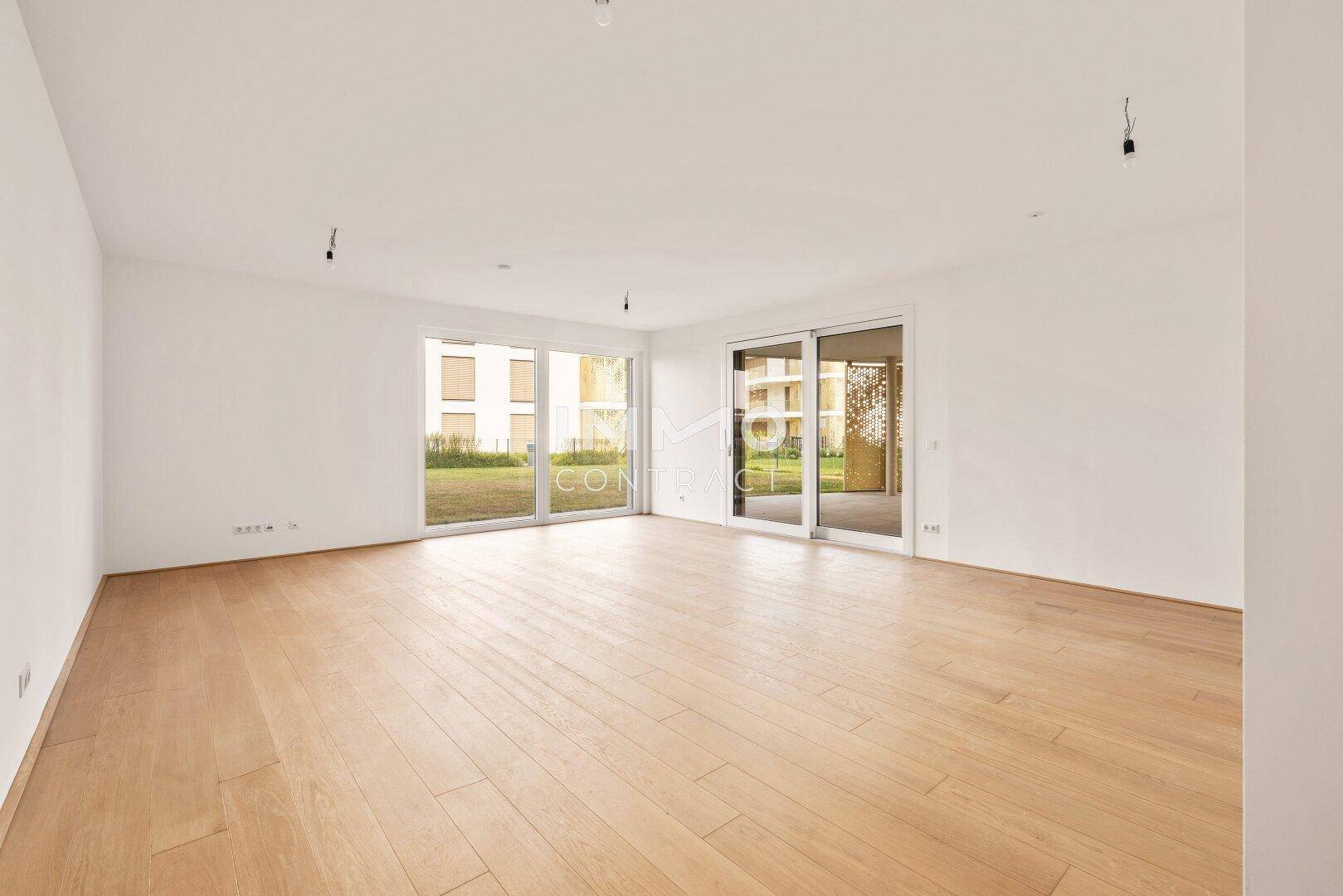 Heller, leerer Wohnraum mit Eichenparkettboden und großen Fenstern zum Garten.