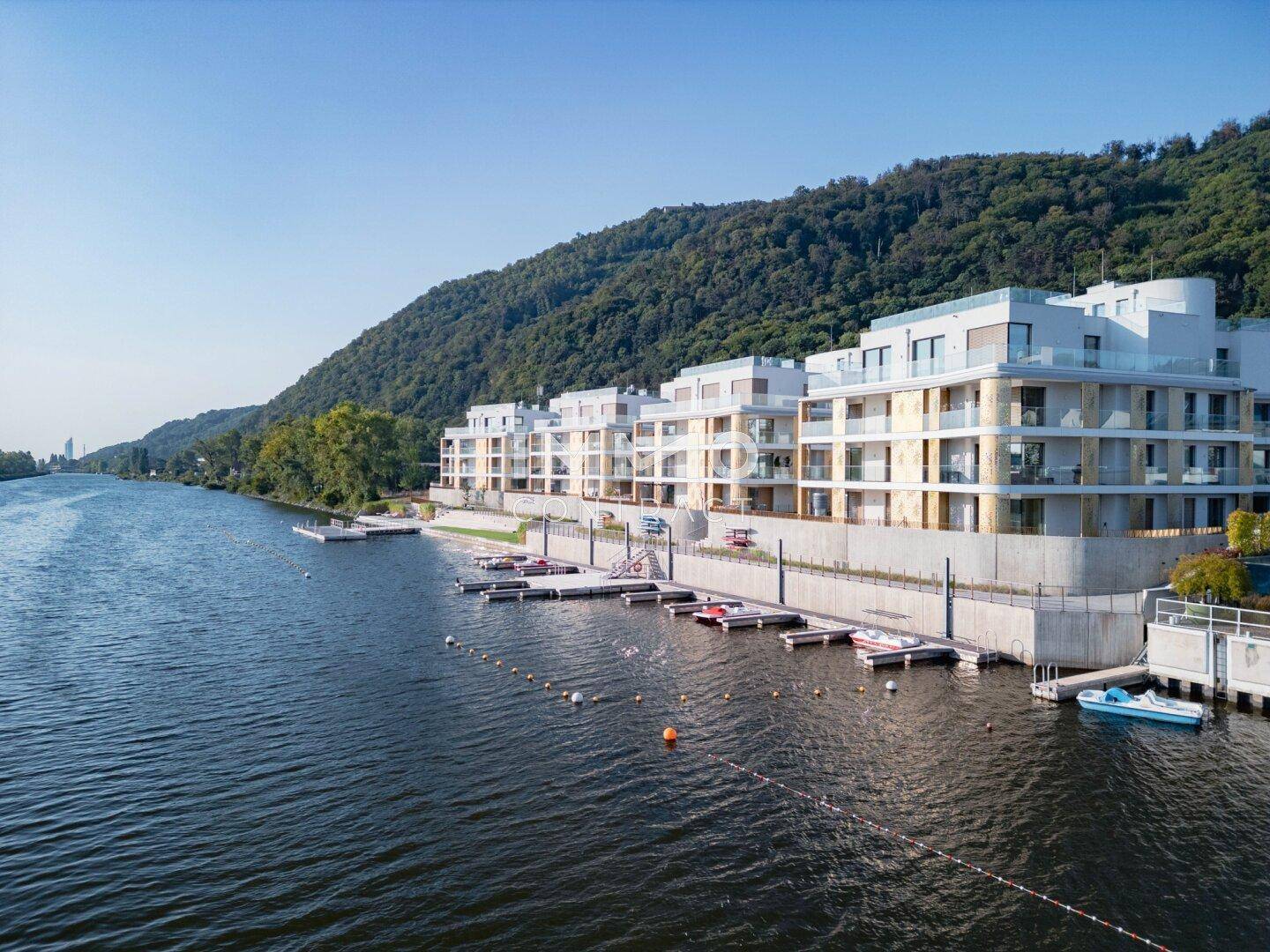 Moderne Wohnanlage am Flussufer mit privaten Anlegestellen und Bergblick.