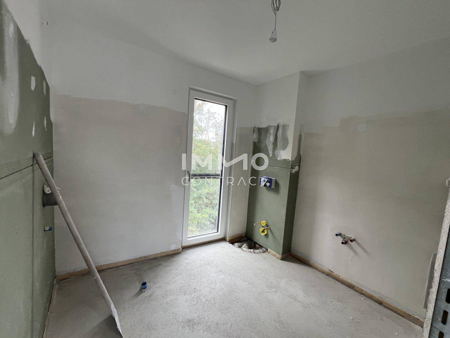 Rohbau-Badezimmer mit vorbereiteten Anschlüssen für Sanitärinstallationen und Fenster.