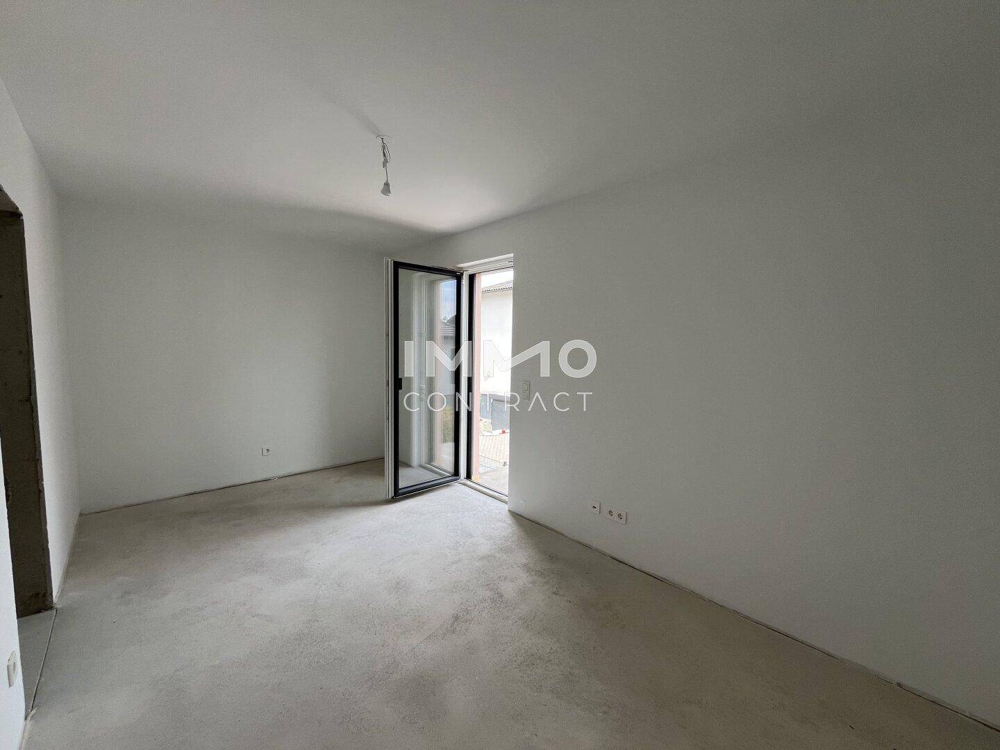Heller Rohbau-Raum mit großer Tür zum Außenbereich und viel Tageslicht.