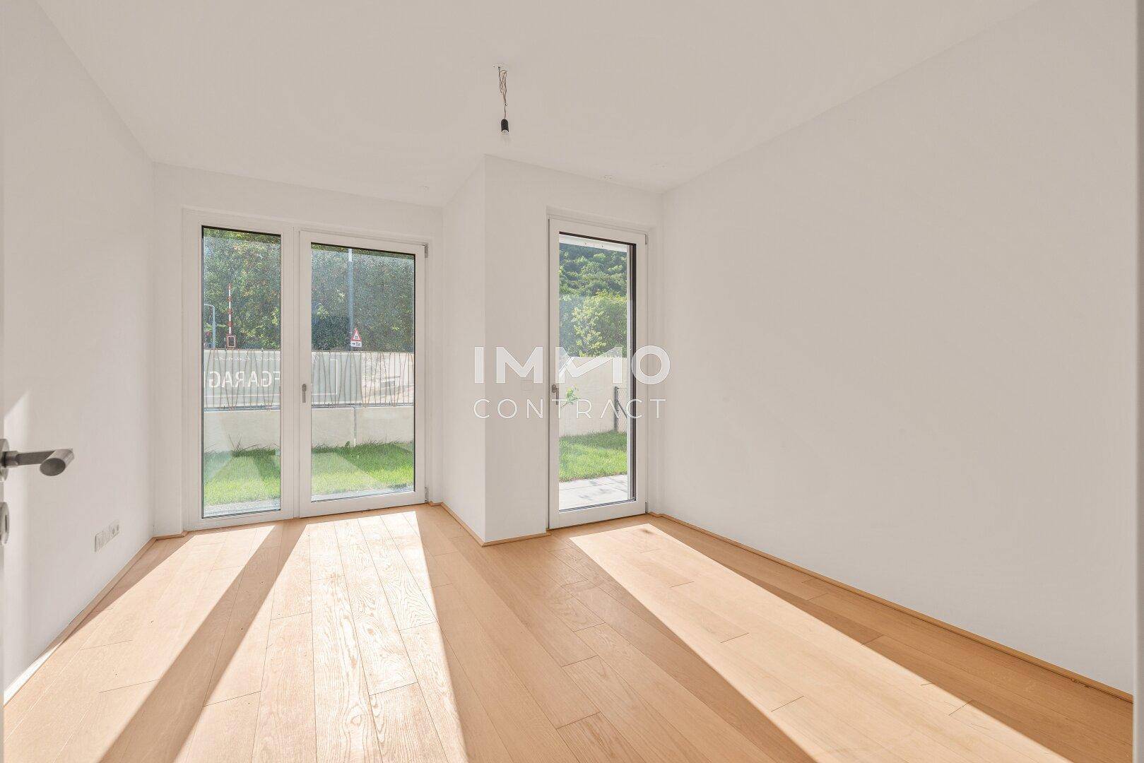 Helles Schlafzimmer mit Parkettboden und großen Fenstern zum Gartenbereich.