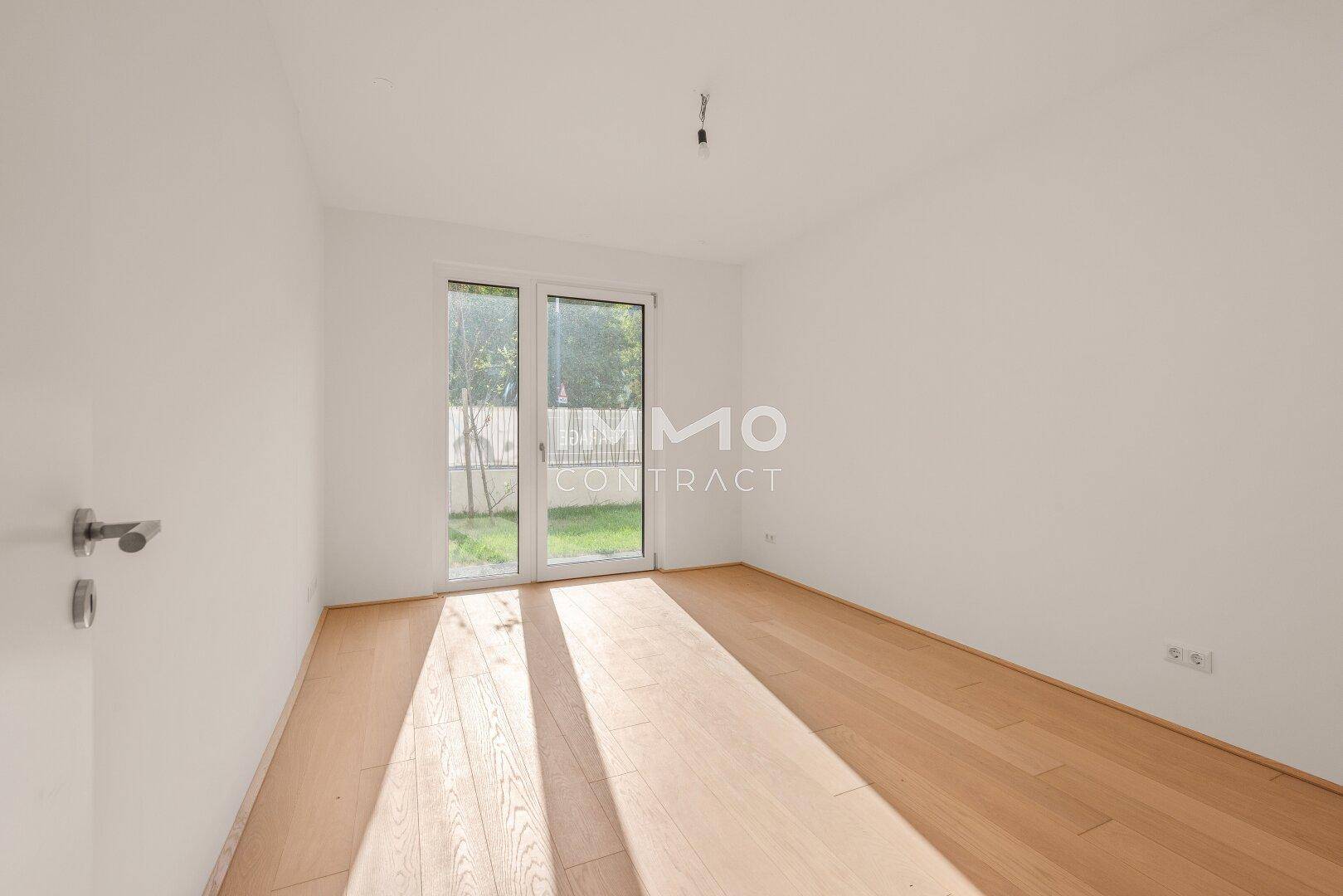 Unmöbliertes Schlafzimmer mit hellem Parkettboden und direktem Zugang zum Garten.