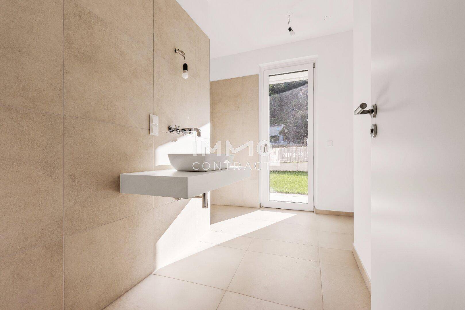Modernes Badezimmer mit beigefarbenen Fliesen, schwebendem Waschbecken und Fenster zum Garten.