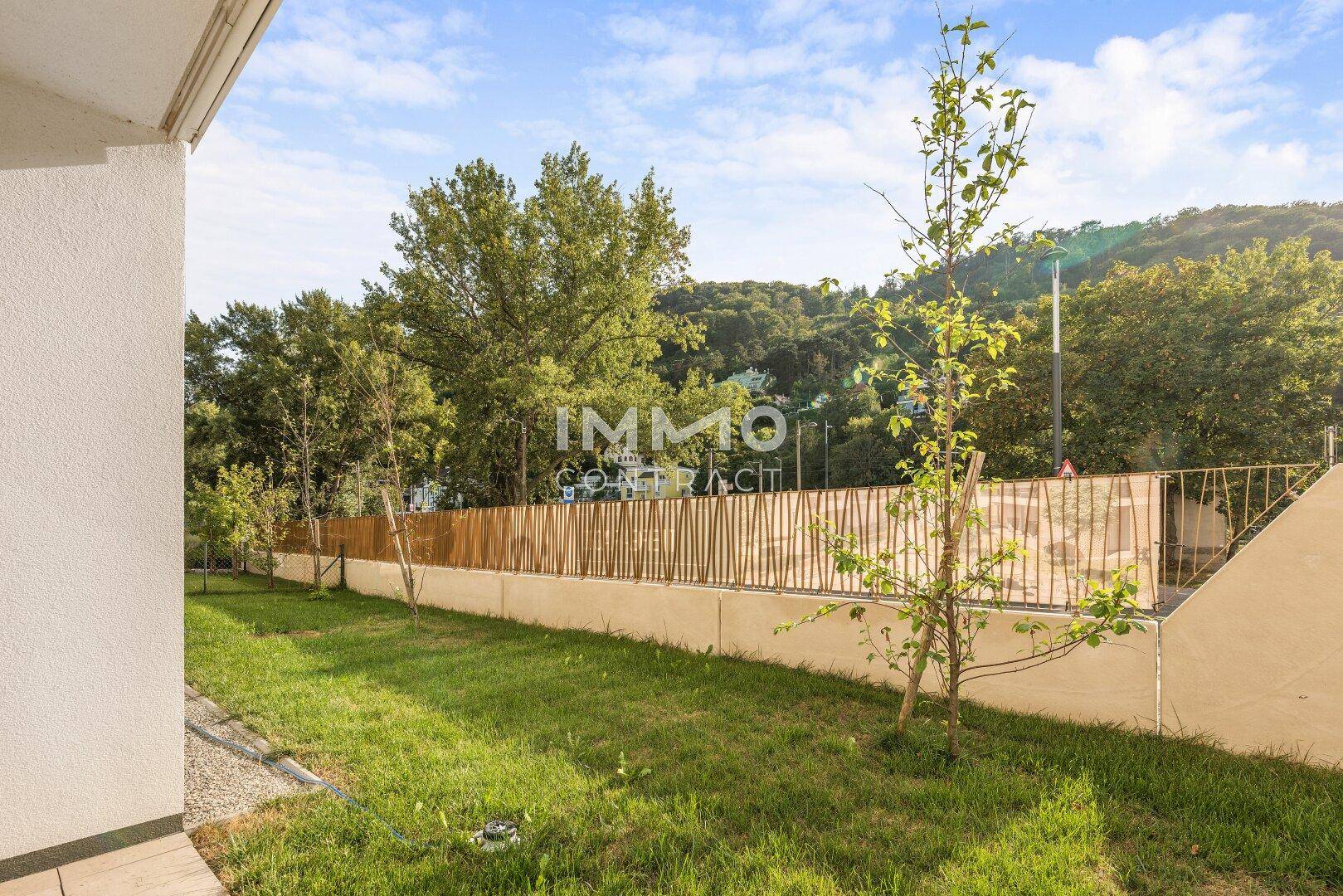 Gepflegter Gartenbereich mit Rasen, Bäumen und einem modernen Zaun im Hintergrund.