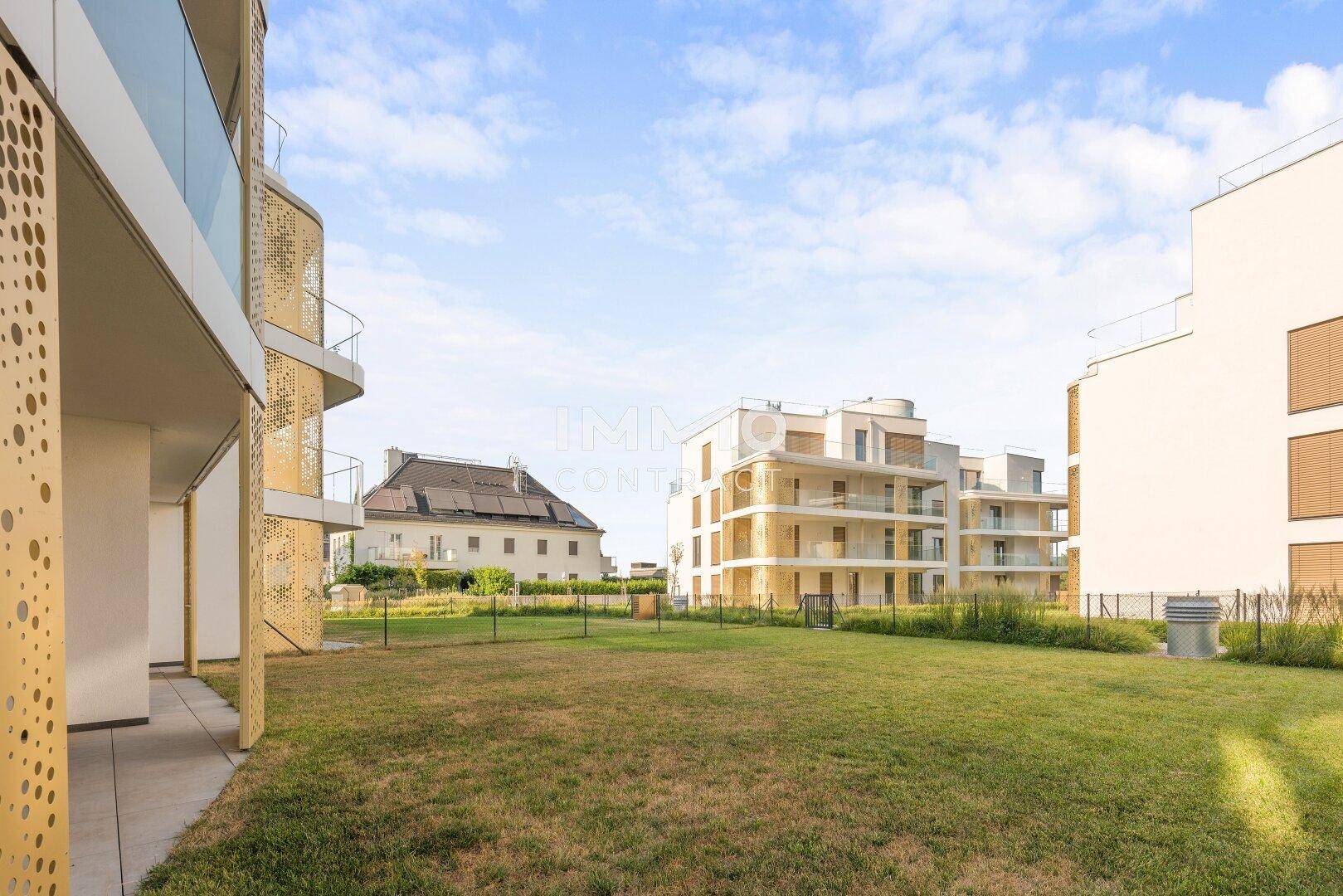 Moderne Wohngebäude umgeben von weitläufigen Grünflächen unter blauem Himmel.