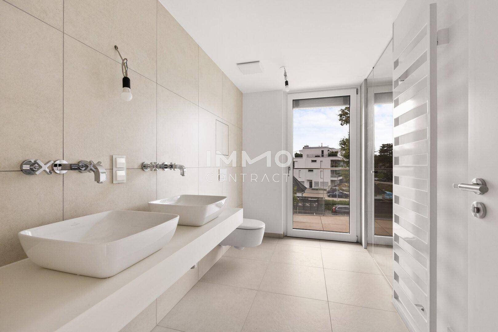 Modernes Badezimmer mit Doppelwaschbecken, Wand-WC und großem Fenster für natürliche Belüftung.