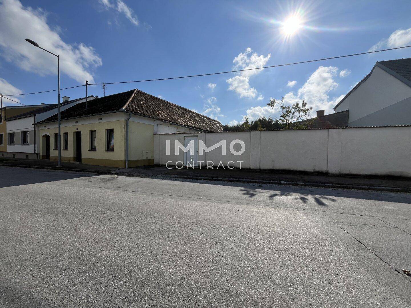 Ansicht eines älteren Wohnhauses von der Straße mit einer hohen Mauer und sonnigem Wetter.