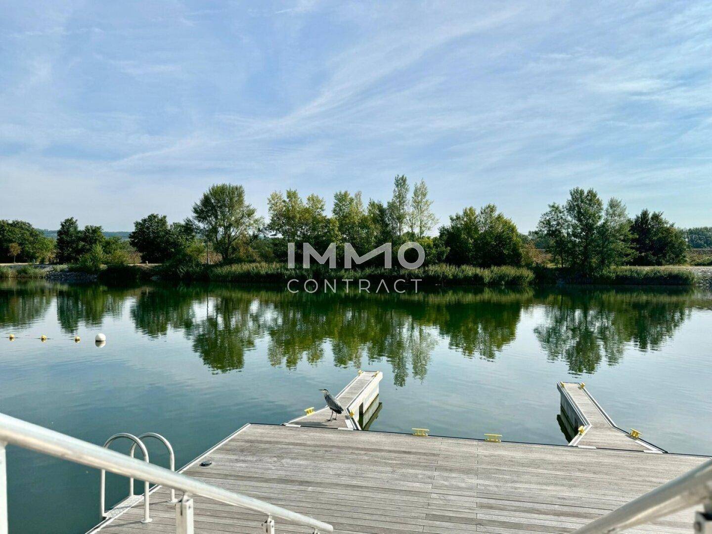 Malerischer See mit Holzstegen und üppiger Vegetation unter blauem Himmel.