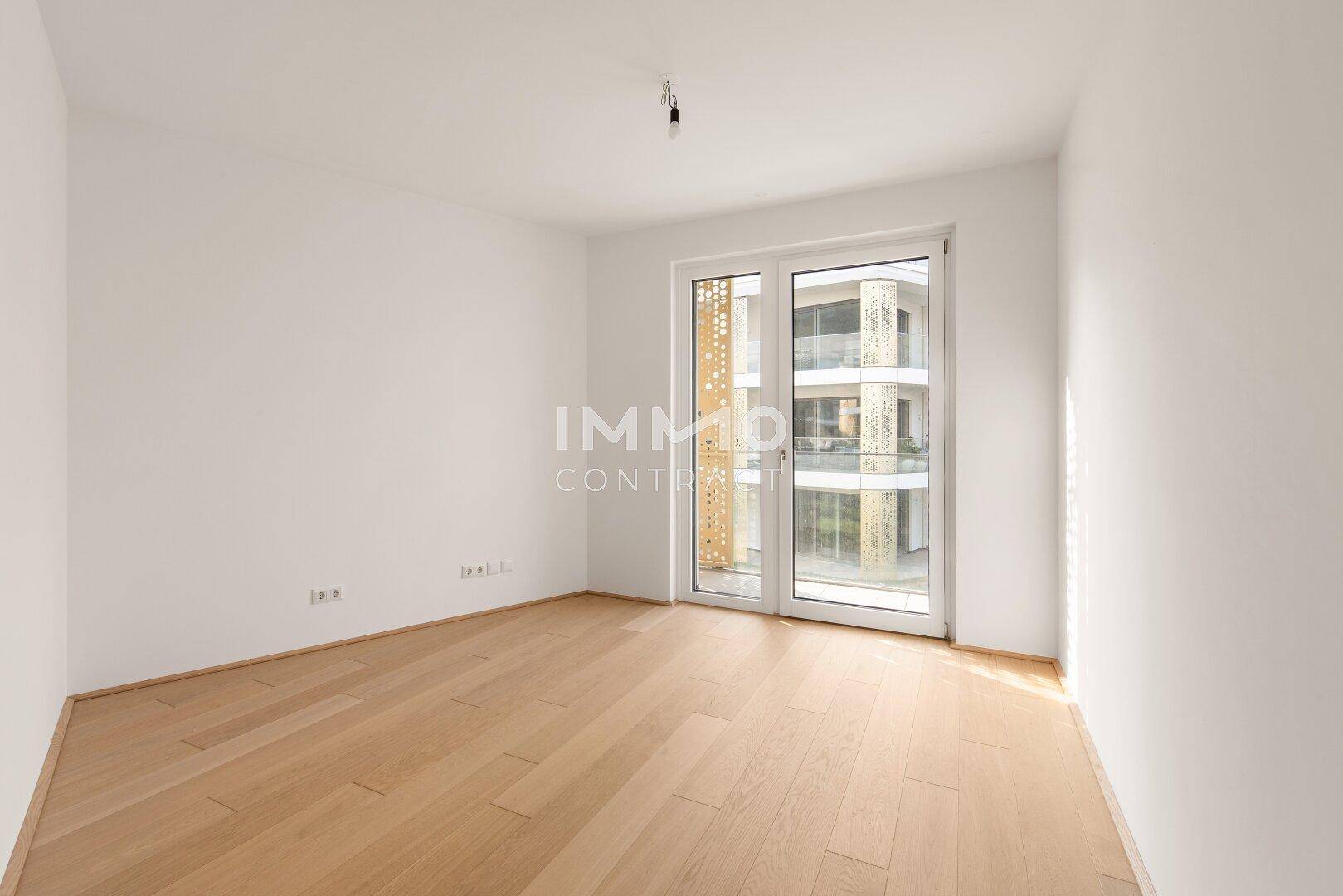 Helles Schlafzimmer mit Parkettboden und Zugang zu einem Balkon, ideal für ein Kinder- oder Gästezimmer.