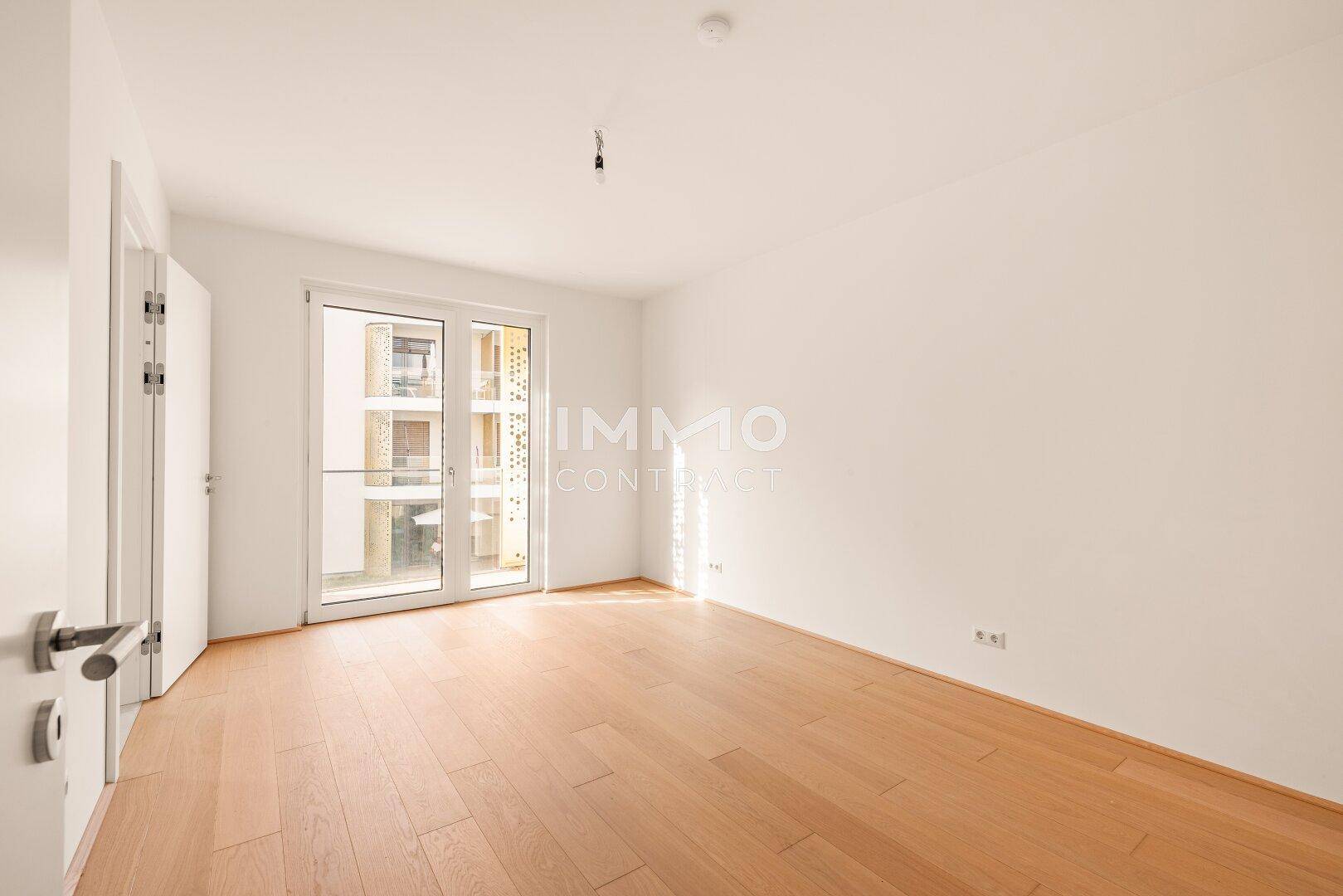 Unmöbliertes Schlafzimmer mit hellem Parkettboden und Balkonzugang, bereit zur individuellen Gestaltung.