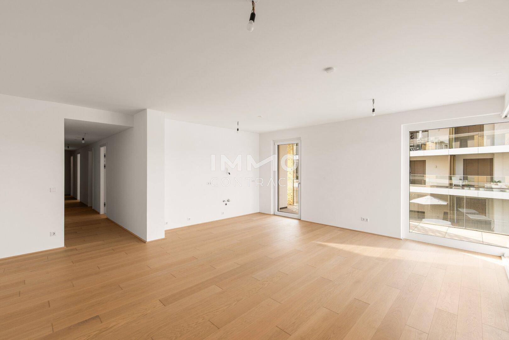 Geräumiges, unmöbliertes Wohnzimmer mit hellem Parkettboden und Zugang zu einem Balkon.