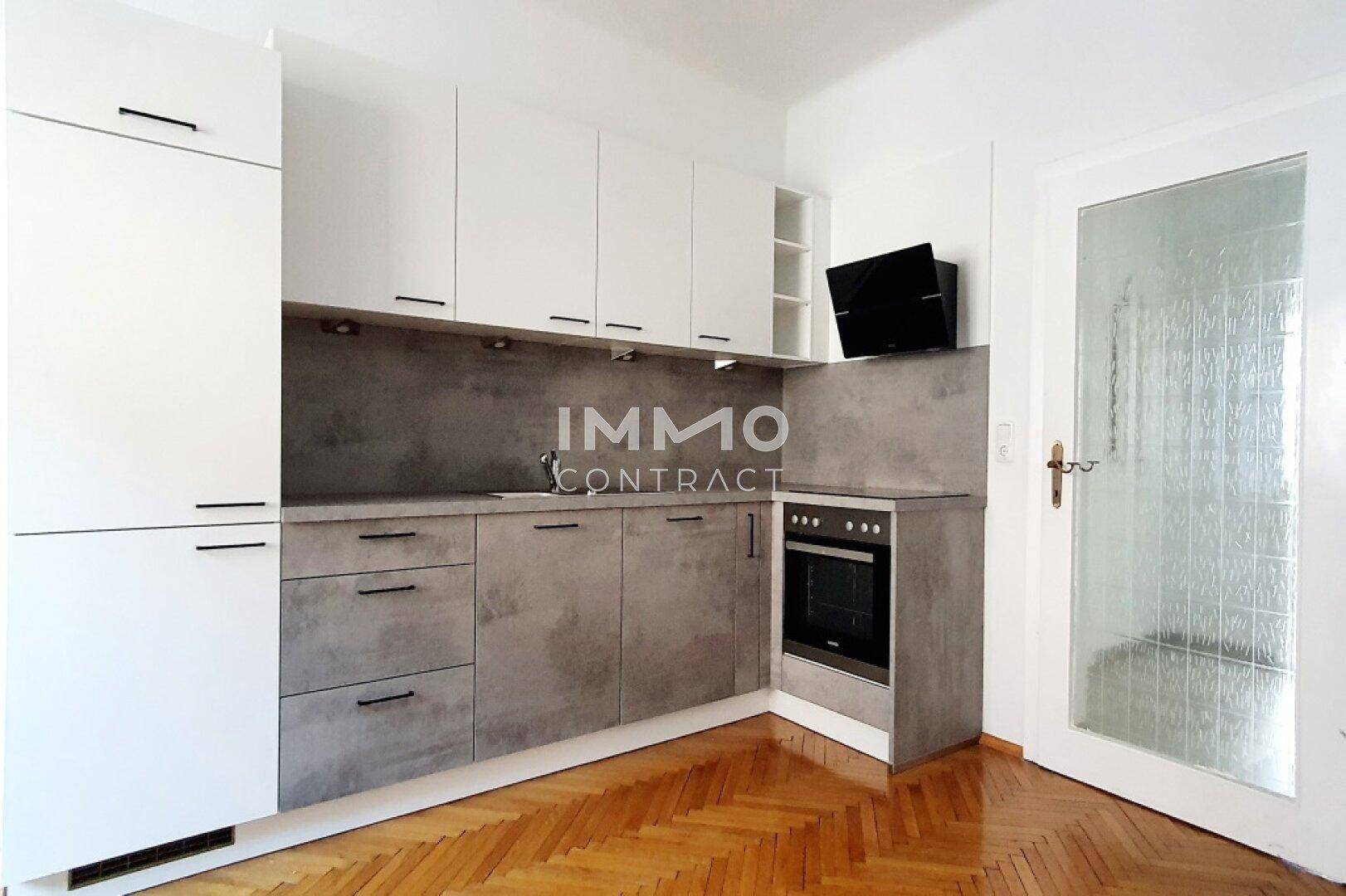 Moderne Einbauküche mit weißen und grauen Schränken sowie Fischgrätparkettboden.