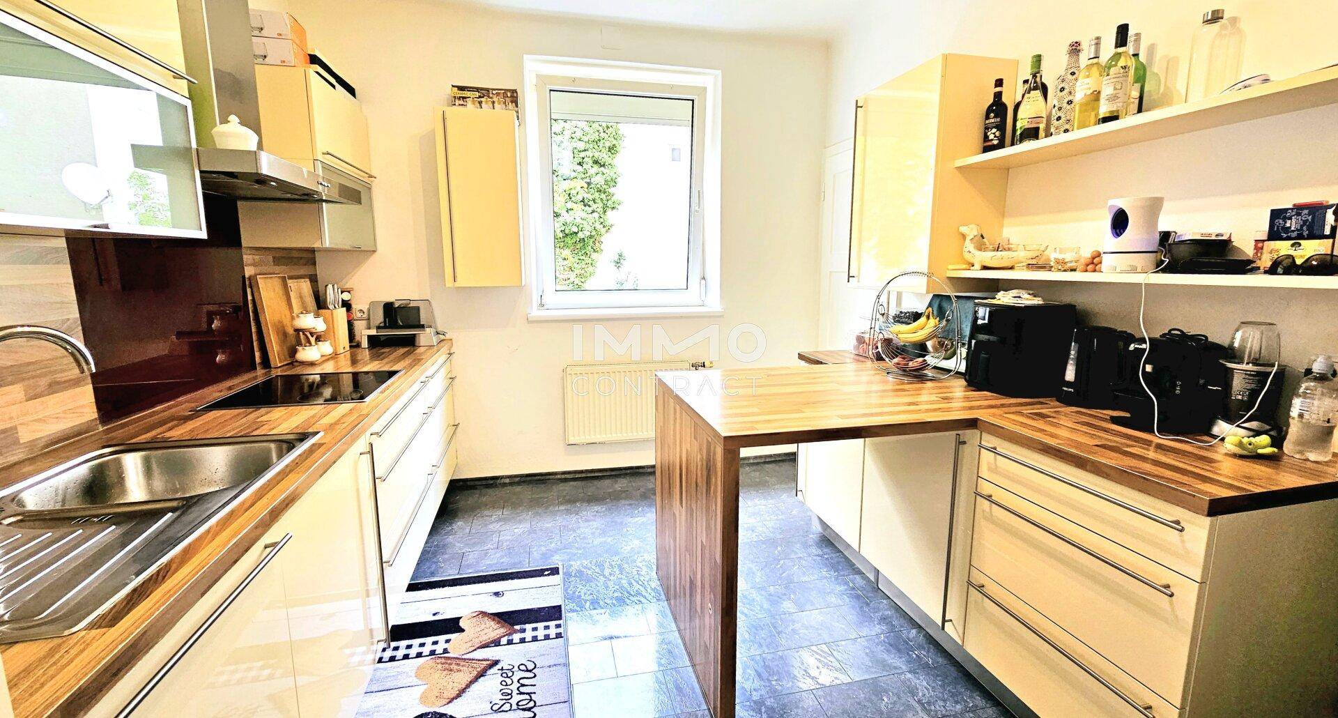 Helle Küche mit Holz-Arbeitsplatten, modernen Geräten und Fensterblick ins Grüne.