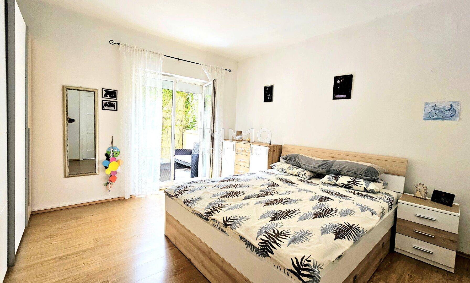 Helles Schlafzimmer mit Holzboden, Doppelbett und Zugang zu einem Balkon.