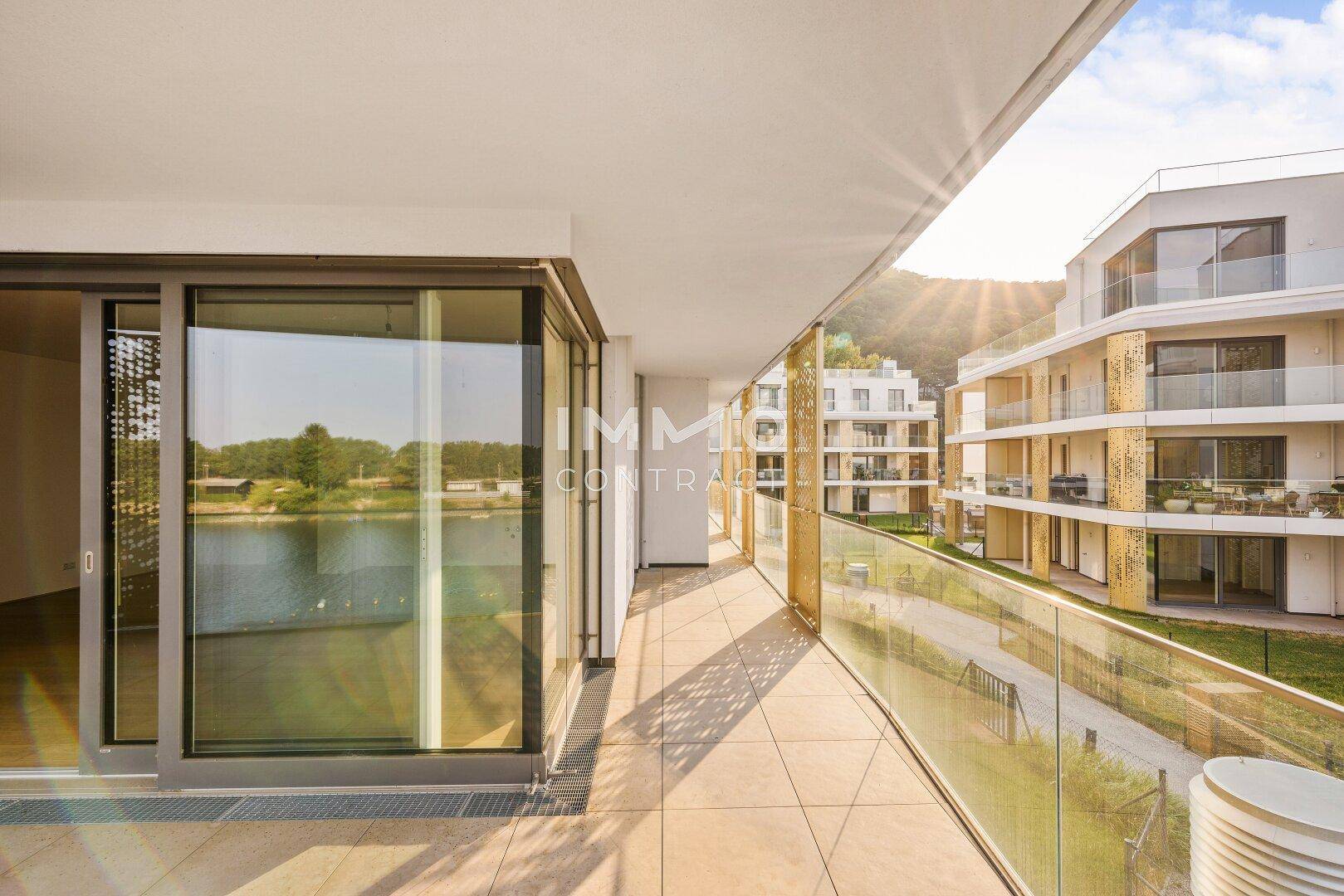 Heller Balkon mit Fliesenboden und Panoramablick auf den See und die gegenüberliegenden Gebäude.