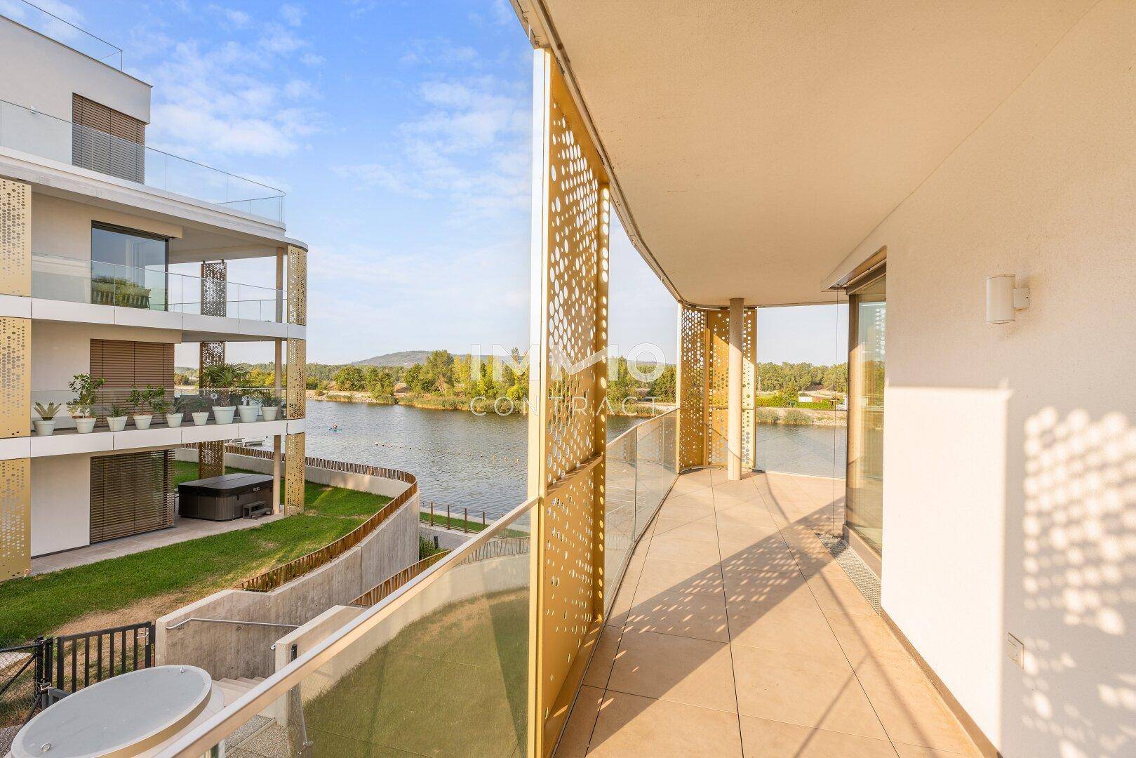 Langer Balkon mit Seeblick, Glasgeländer und dekorativen goldenen Paneelen an der Fassade.