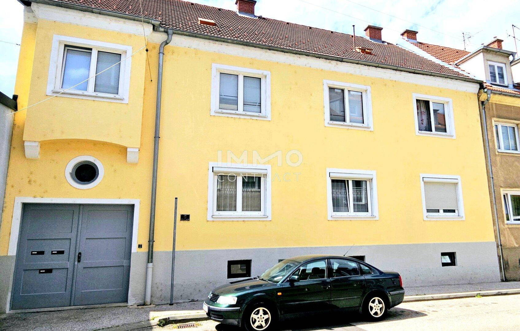 Gelbe Fassade eines Mehrfamilienhauses mit Garagentor und Fenstern zur Straße.