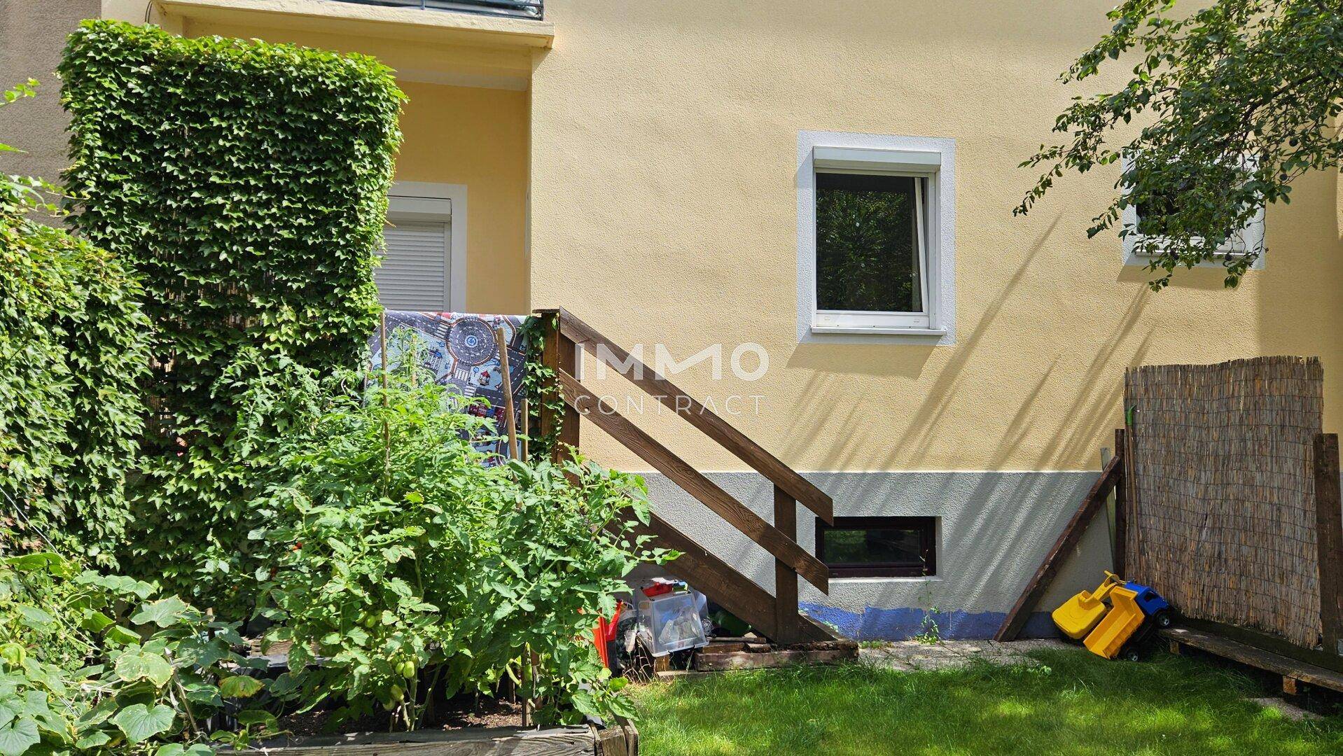 Detailansicht des Gartens mit üppigem Grün, Kletterpflanzen und Holztreppe zum Haus.