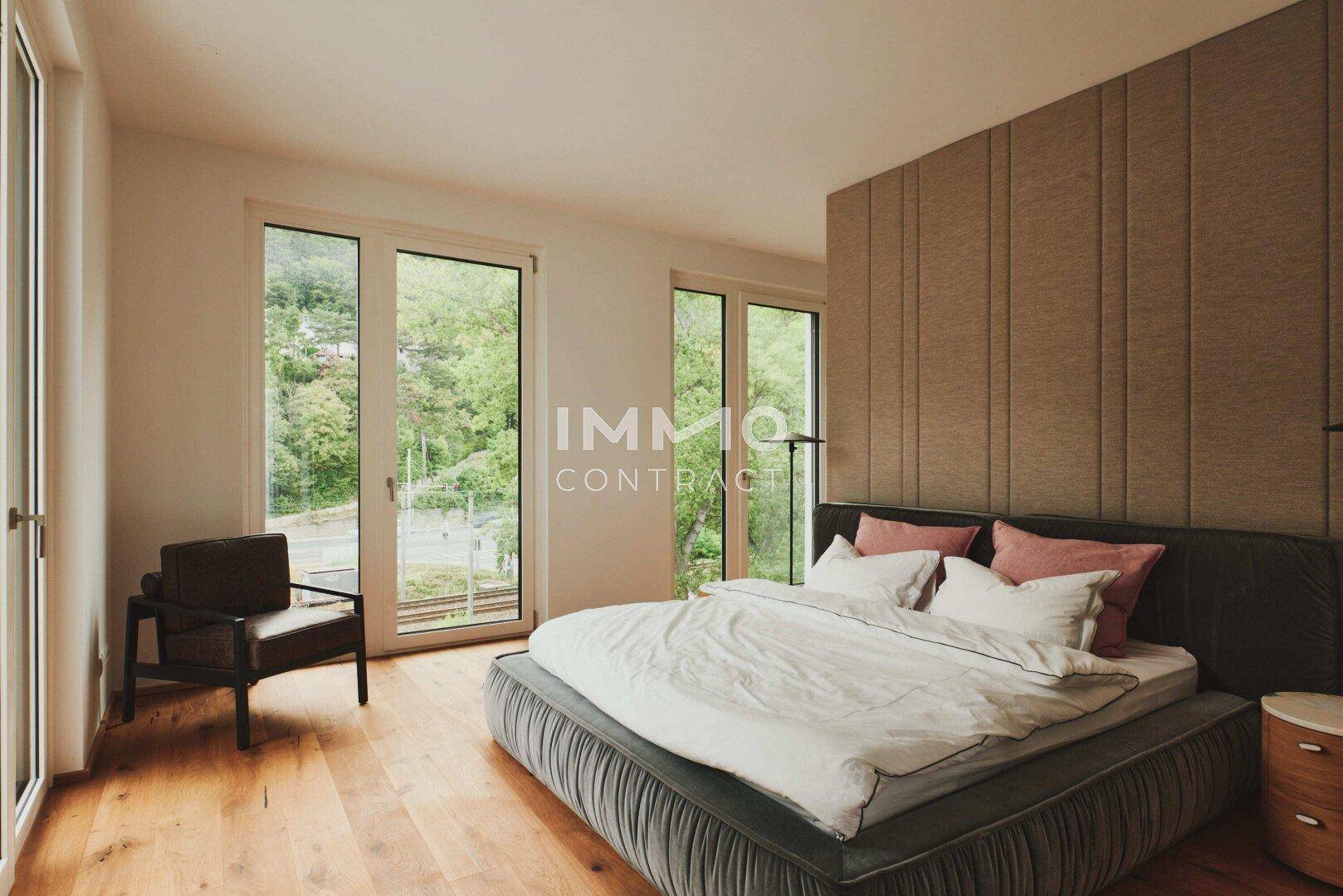 Schlafzimmer mit großen Fenstern, die viel Tageslicht und einen grünen Ausblick bieten.