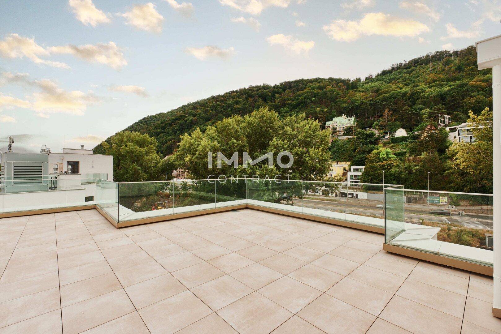 Große Terrasse mit Glasgeländer und einem malerischen Blick auf bewaldete Hügel.