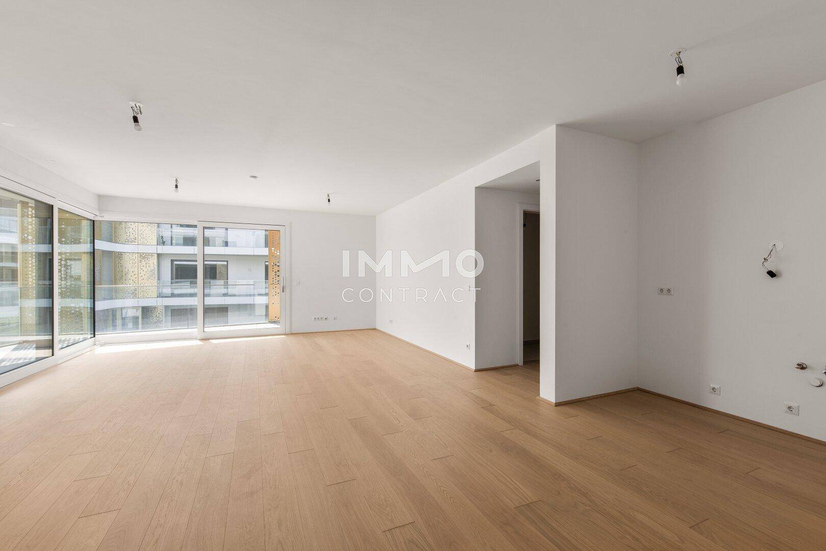 Heller, leerer Raum mit großen Fenstern und hellem Holzparkett, ideal für einen Wohnbereich.