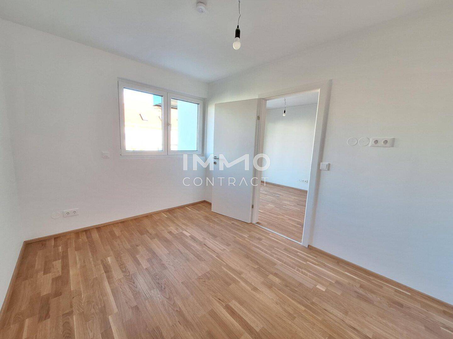 Leeres Schlafzimmer mit hellem Parkettboden und Fenster, das viel Tageslicht hereinlässt.
