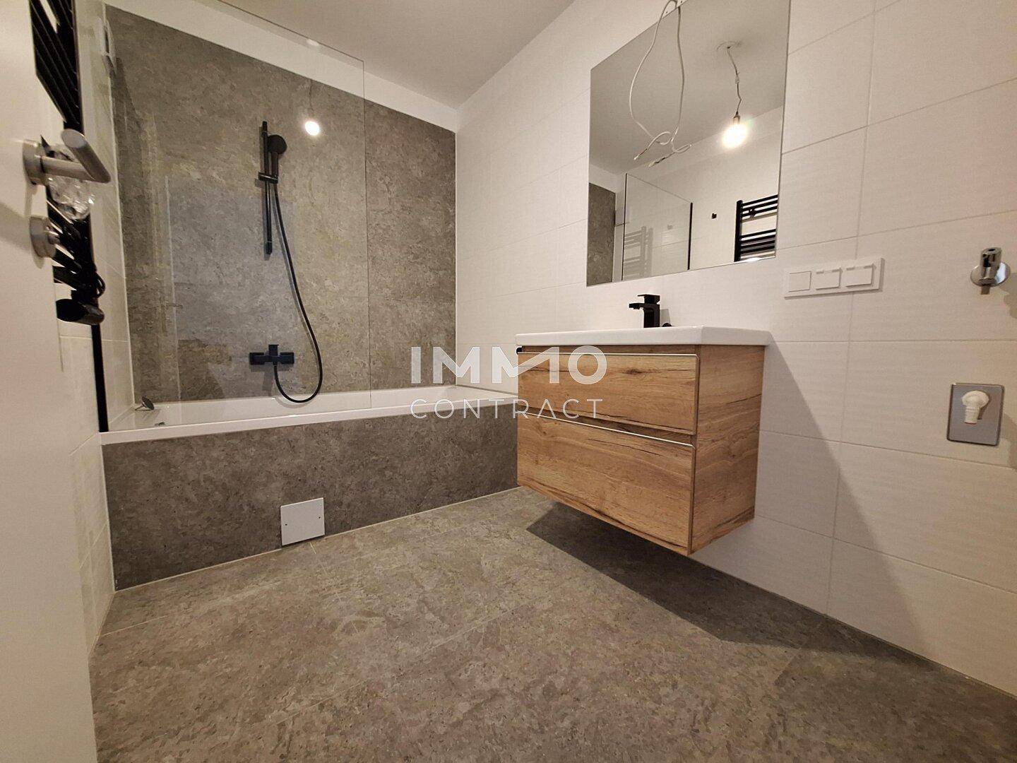 Modernes Badezimmer mit Badewanne, schwebendem Waschtisch und dunklen Fliesenakzenten.