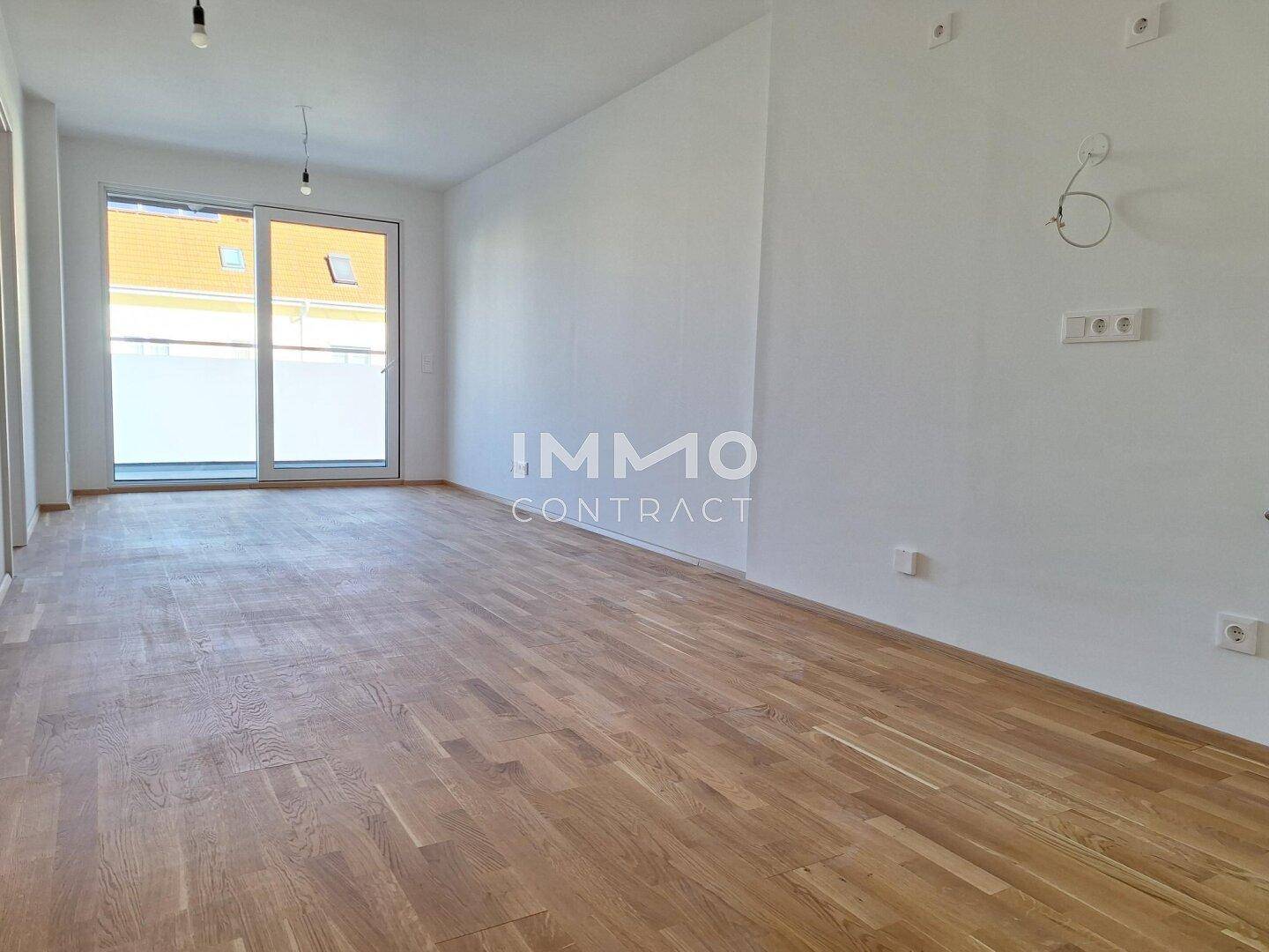 Heller, leerer Wohnraum mit neuem Parkettboden und Zugang zu einem Balkon.