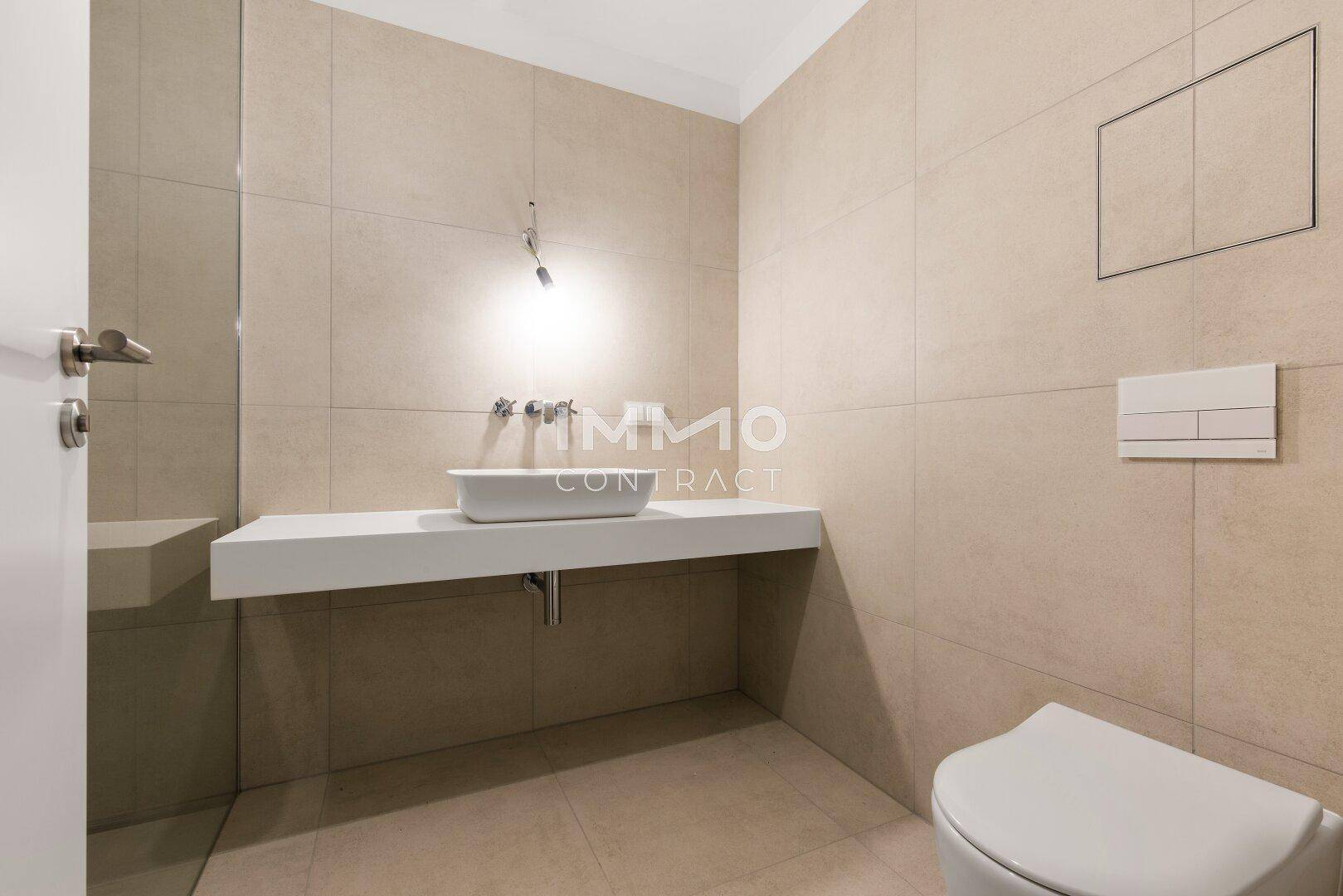 Modernes Gäste-WC mit beigefarbenen Fliesen, einem wandmontierten Waschbecken und Toilette.