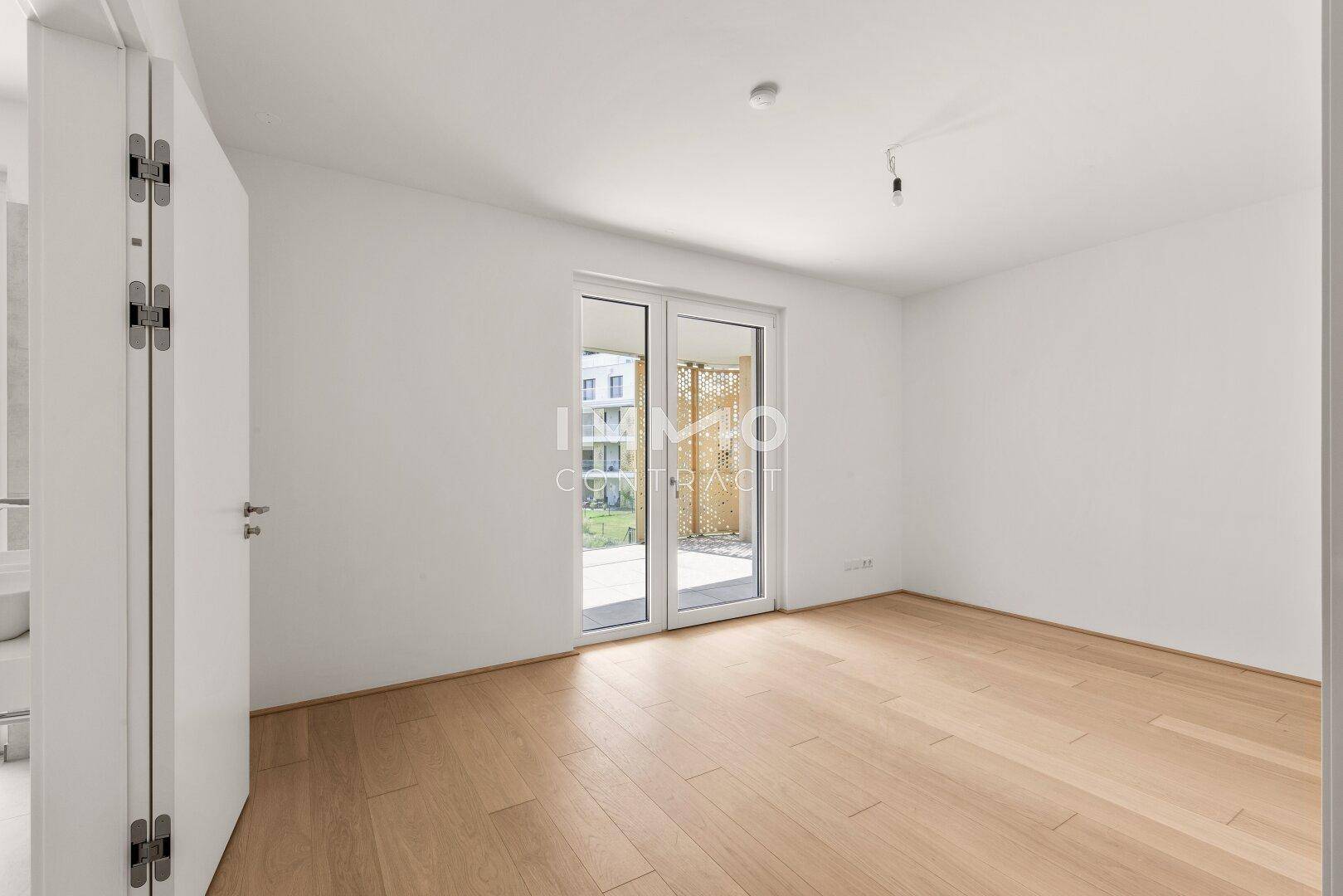 Geräumiges Schlafzimmer mit hellem Holzparkett und Zugang zu einem Außenbereich.