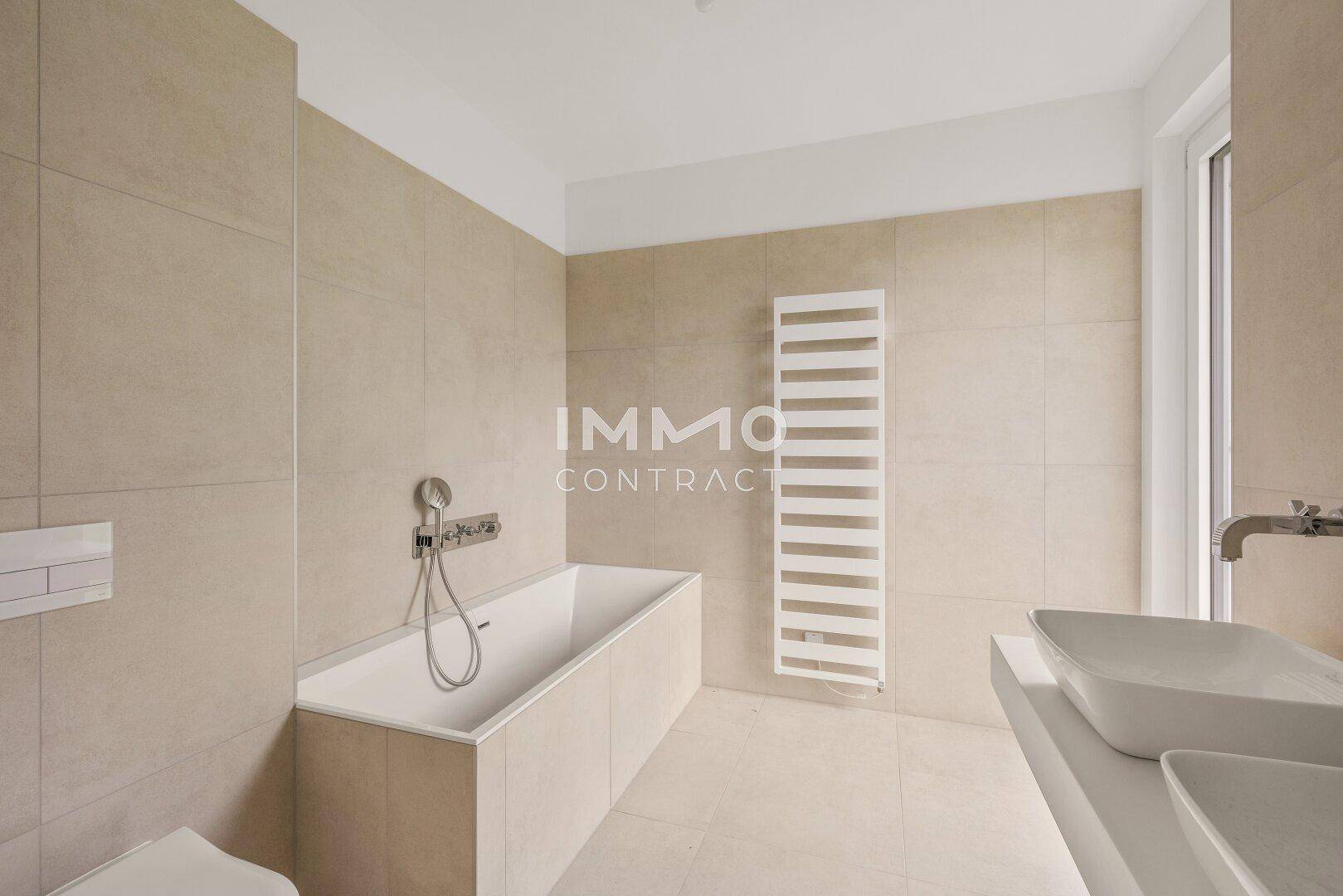 Modernes Badezimmer mit beigefarbenen Fliesen, einer Badewanne, Doppelwaschbecken und Handtuchheizkörper.
