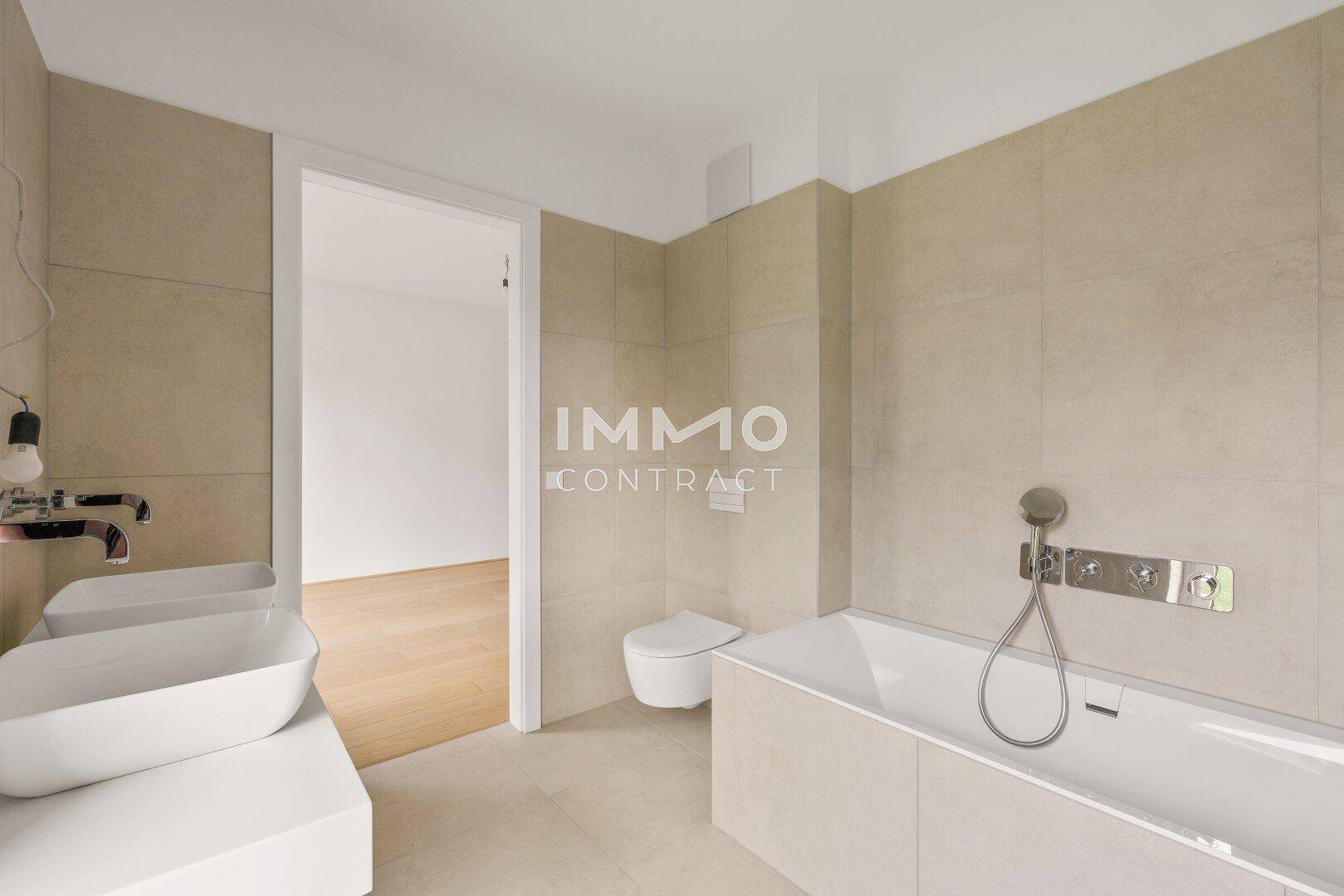 Geräumiges Badezimmer mit beigefarbenen Fliesen, Badewanne, Doppelwaschbecken und Zugang zu einem weiteren Raum.