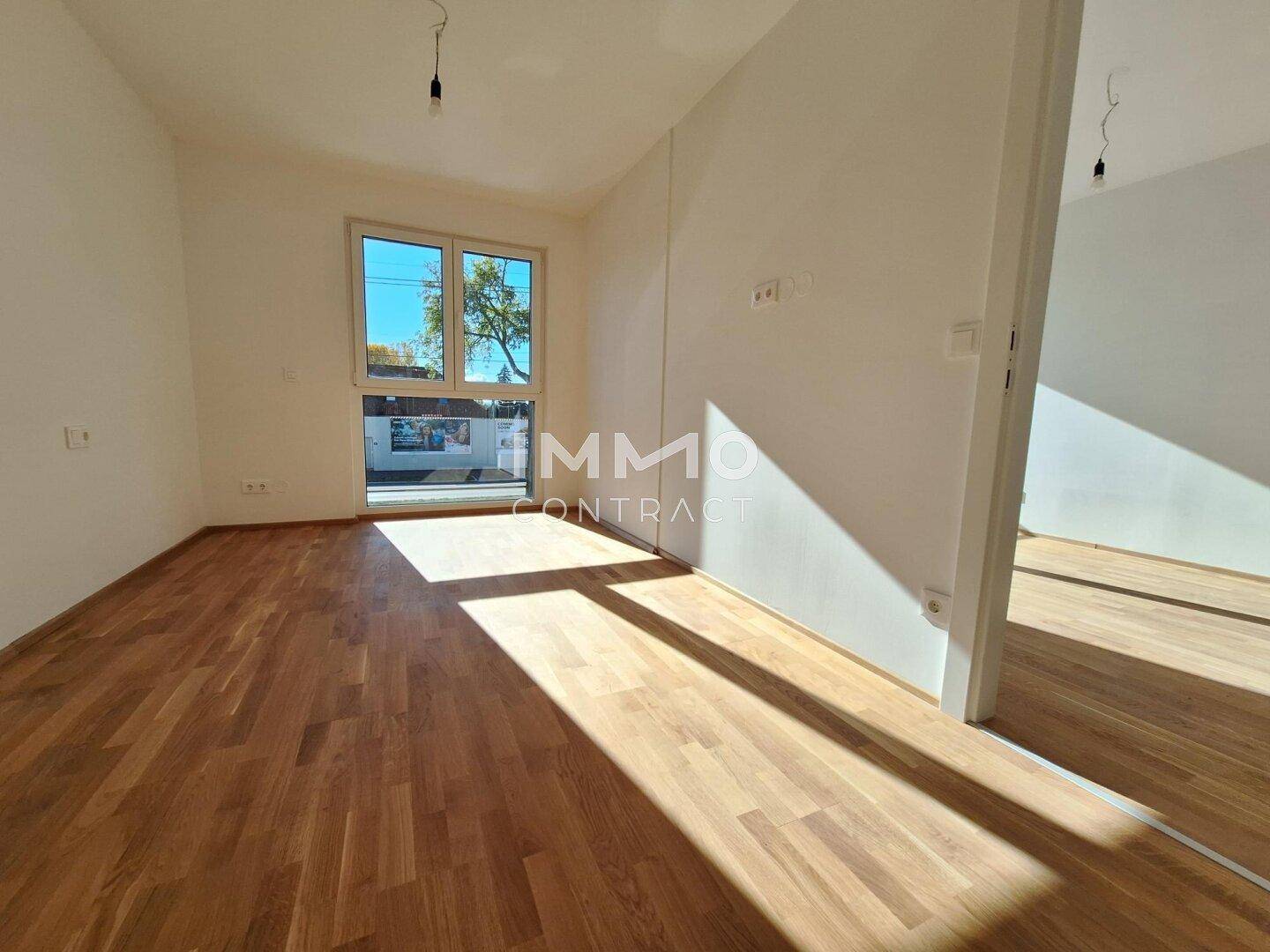 Leeres Zimmer mit hellem Parkettboden und einem großen Fenster, das den Raum mit natürlichem Licht füllt.