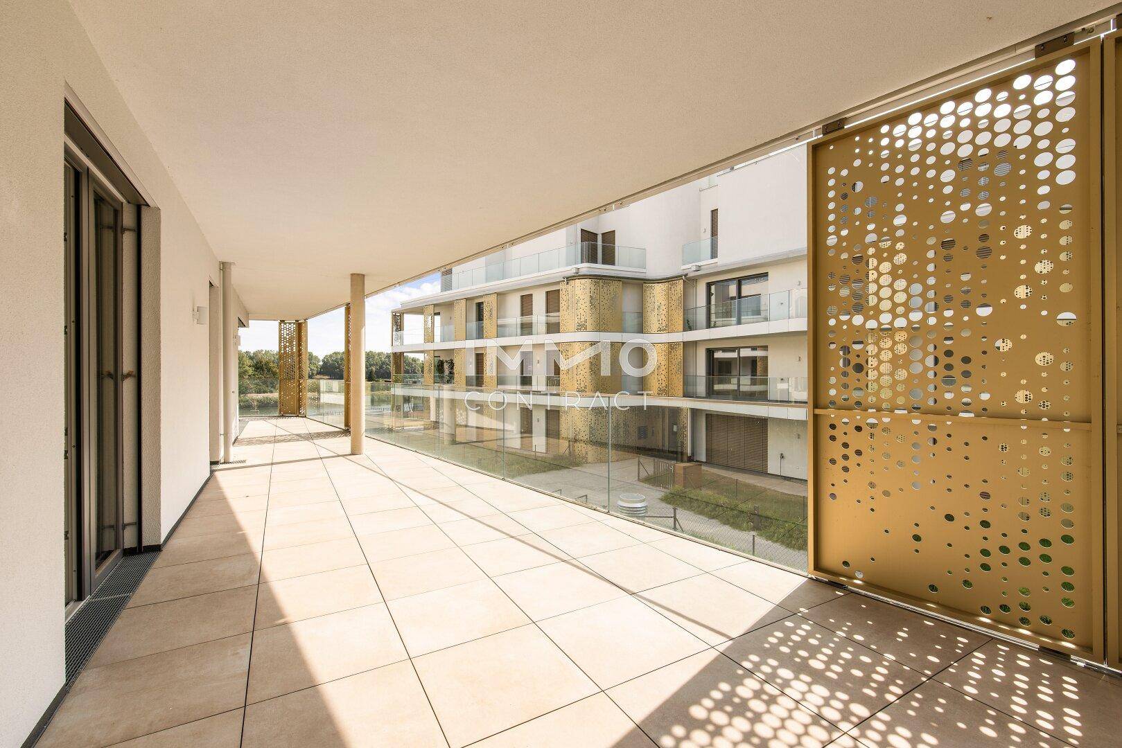 Langer, gefliester Balkon mit modernen Sichtschutz-Elementen und Blick auf die Wohnanlage.