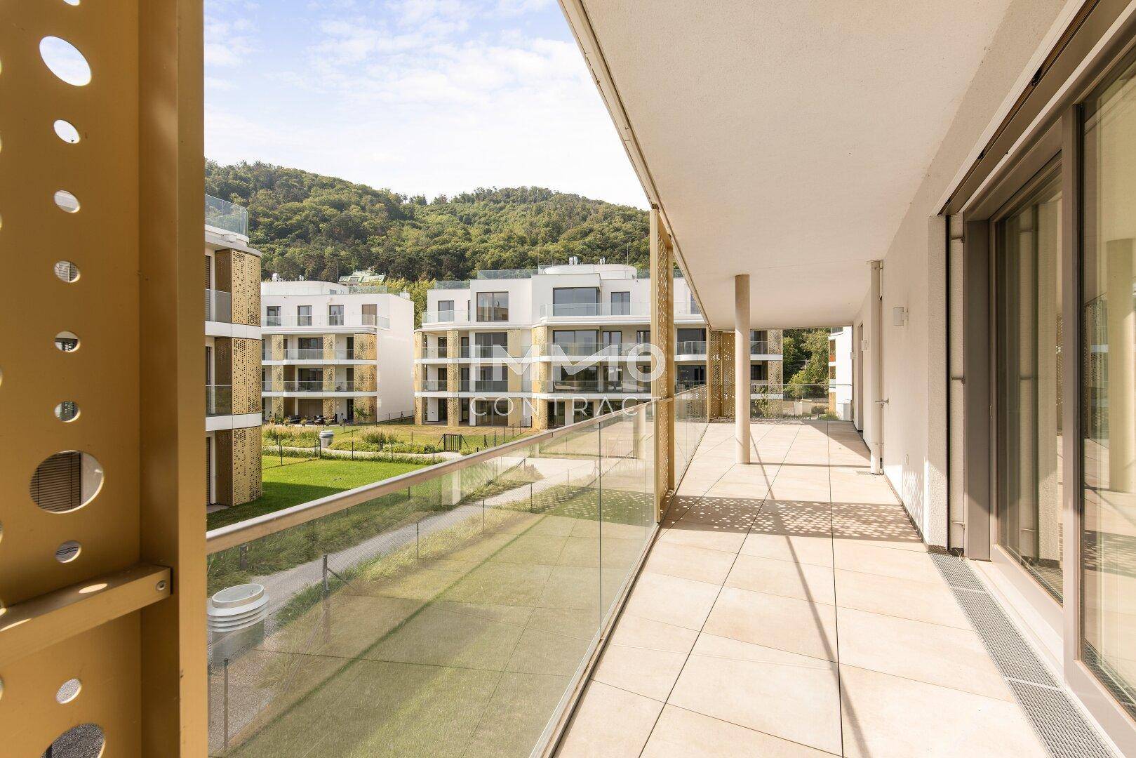 Großer Balkon mit Fliesenboden, Glasgeländer und weitem Blick auf die Umgebung und Berge.