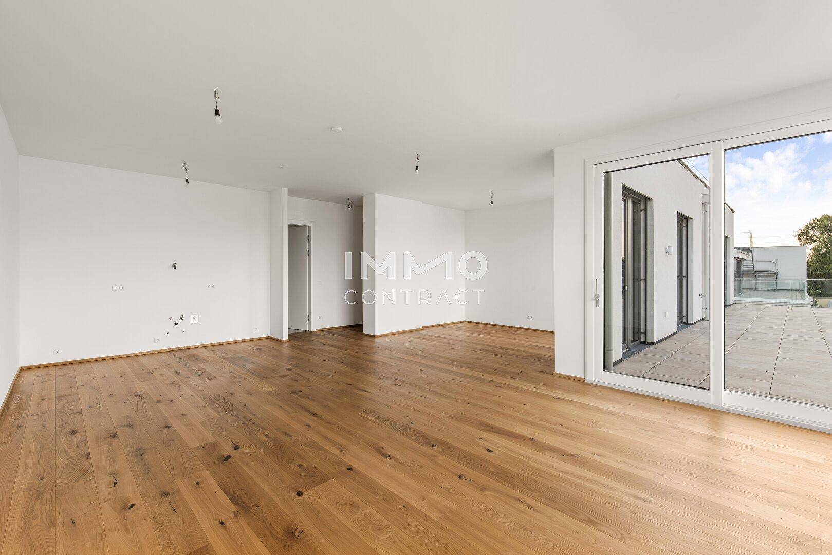 Weitläufiges Wohnzimmer mit Holzboden und Zugang zu einer großen Außenterrasse.