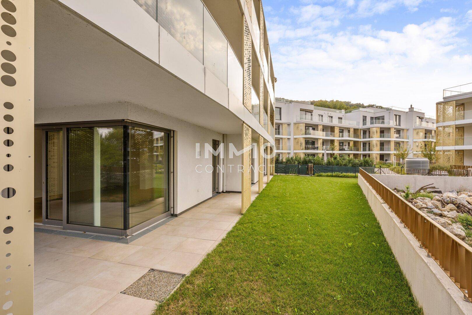 Moderne Gebäudefassade mit Terrassenbereich, Rasenfläche und großen Glasfronten im Erdgeschoss.