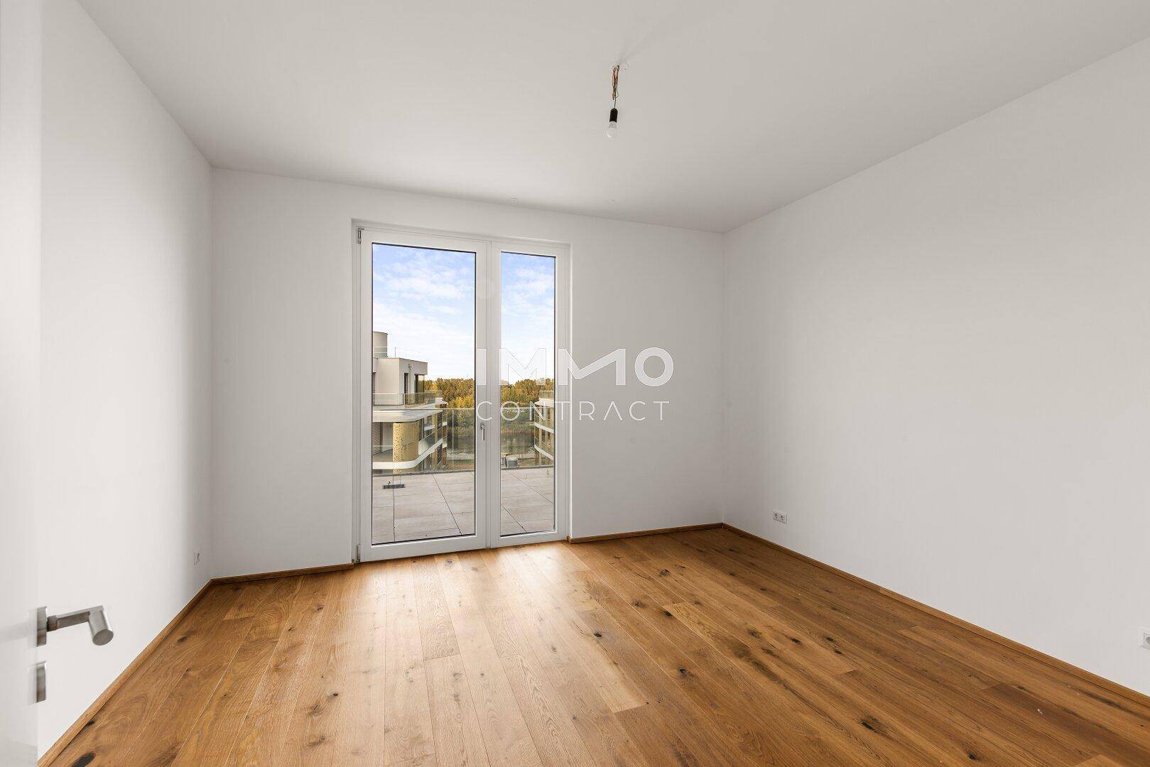 Helles Schlafzimmer mit Holzboden und Zugang zu einem Balkon oder einer Terrasse.