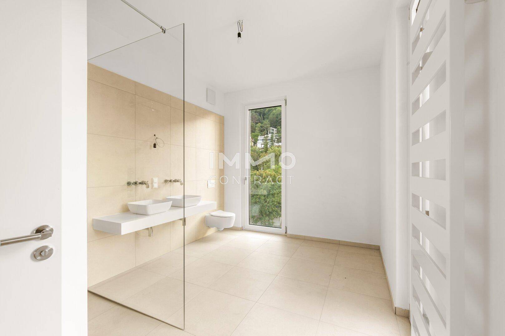Modernes Badezimmer mit begehbarer Dusche, Doppelwaschbecken und Fenster mit Grünblick.