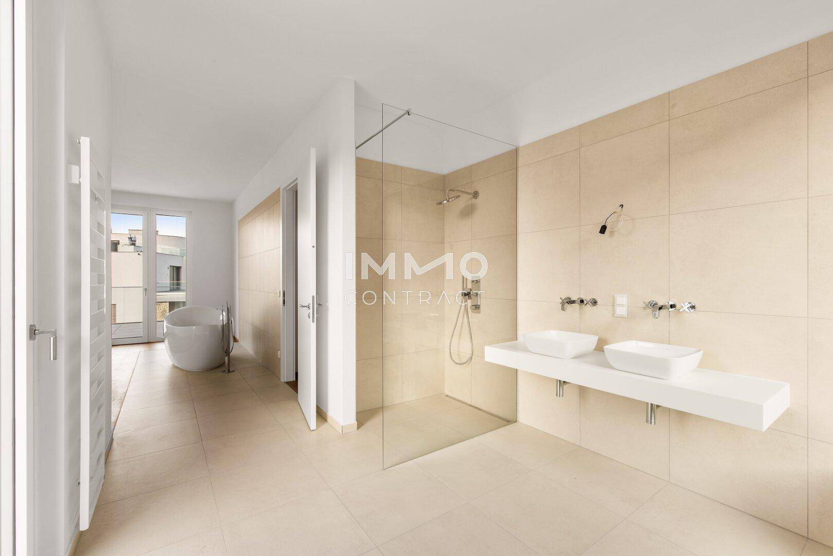 Großes, modernes Badezimmer mit begehbarer Dusche, Doppelwaschbecken und Zugang zu einem weiteren Raum.