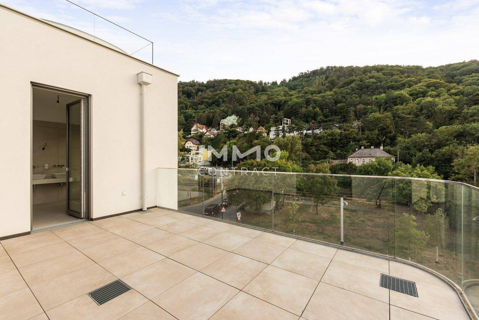 Weitläufige Terrasse mit Fliesenboden und Glasgeländer, bietet Blick auf die Umgebung.