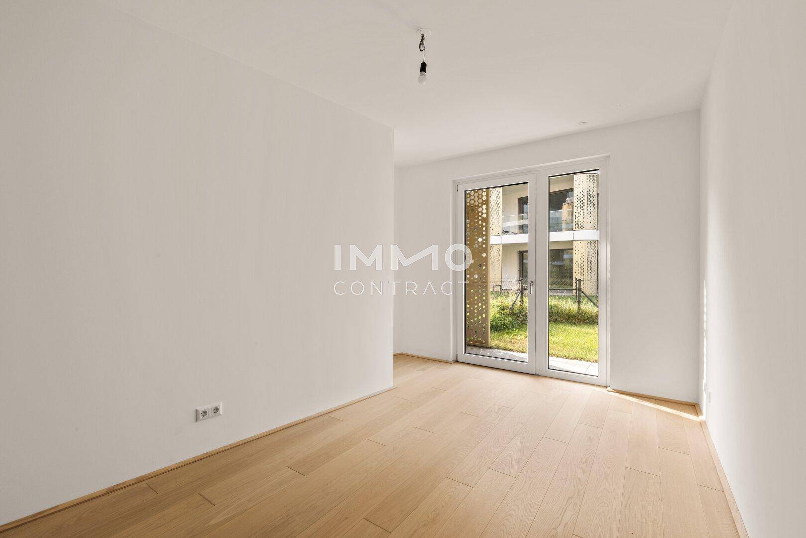 Helles Zimmer mit Holzboden und direktem Zugang zu einer kleinen Grünfläche im Freien.