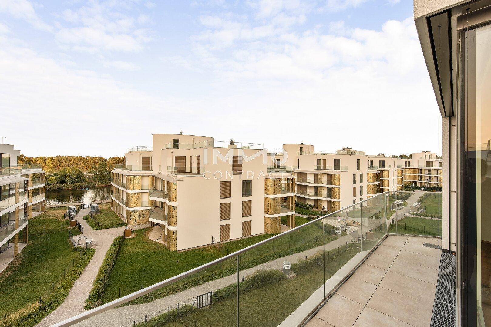 Balkon mit Glasgeländer und Blick auf die modernen Wohngebäude und das Wasser.