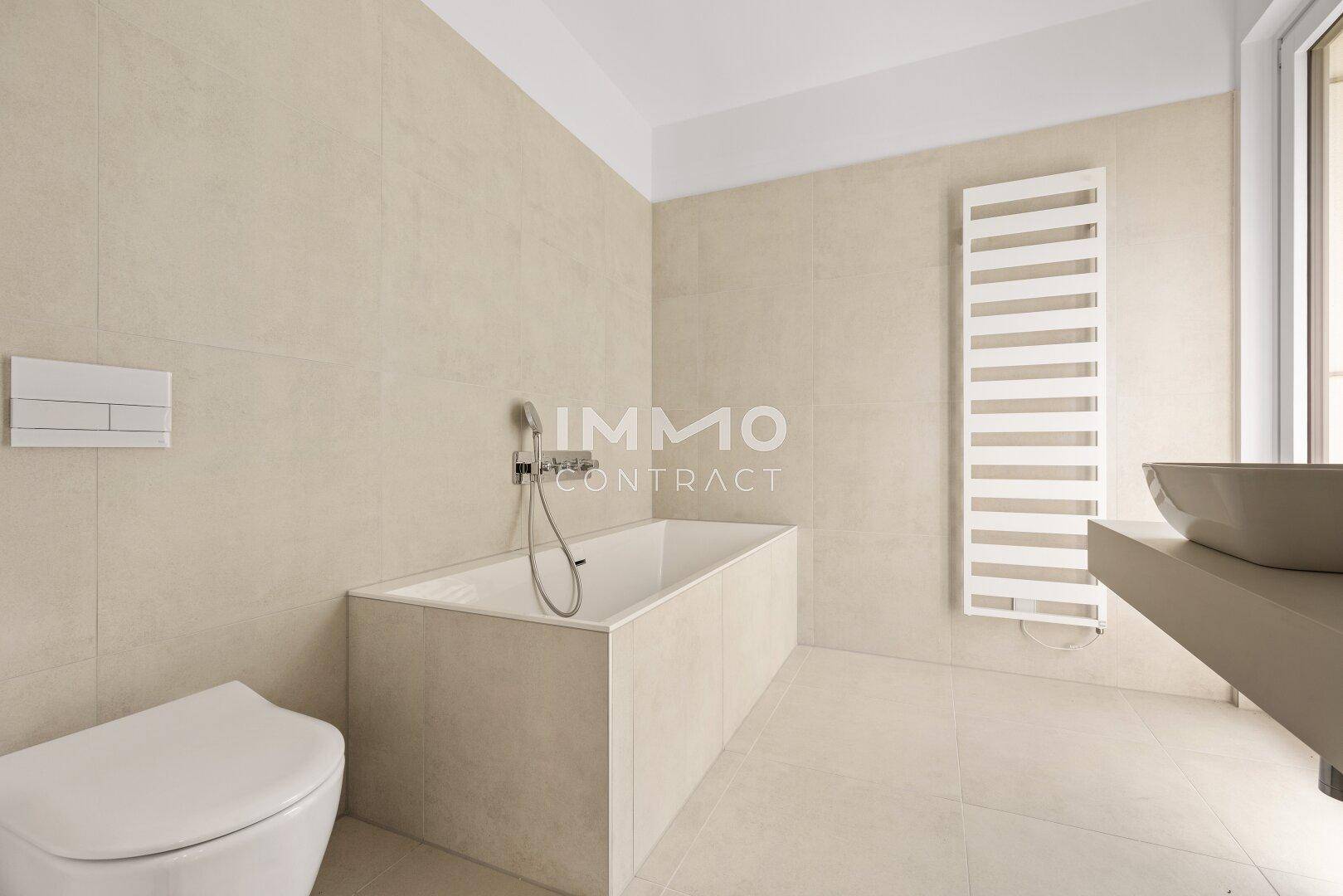 Modernes Badezimmer mit Badewanne, wandhängendem WC, beheiztem Handtuchhalter und beigefarbenen Fliesen.