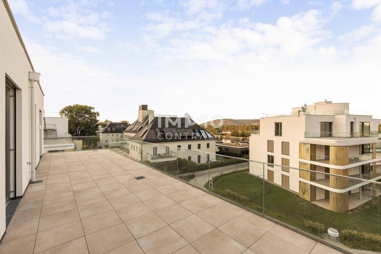Geräumige Terrasse mit Fliesenboden und Glasgeländer, bietet weiten Blick auf die Umgebung.