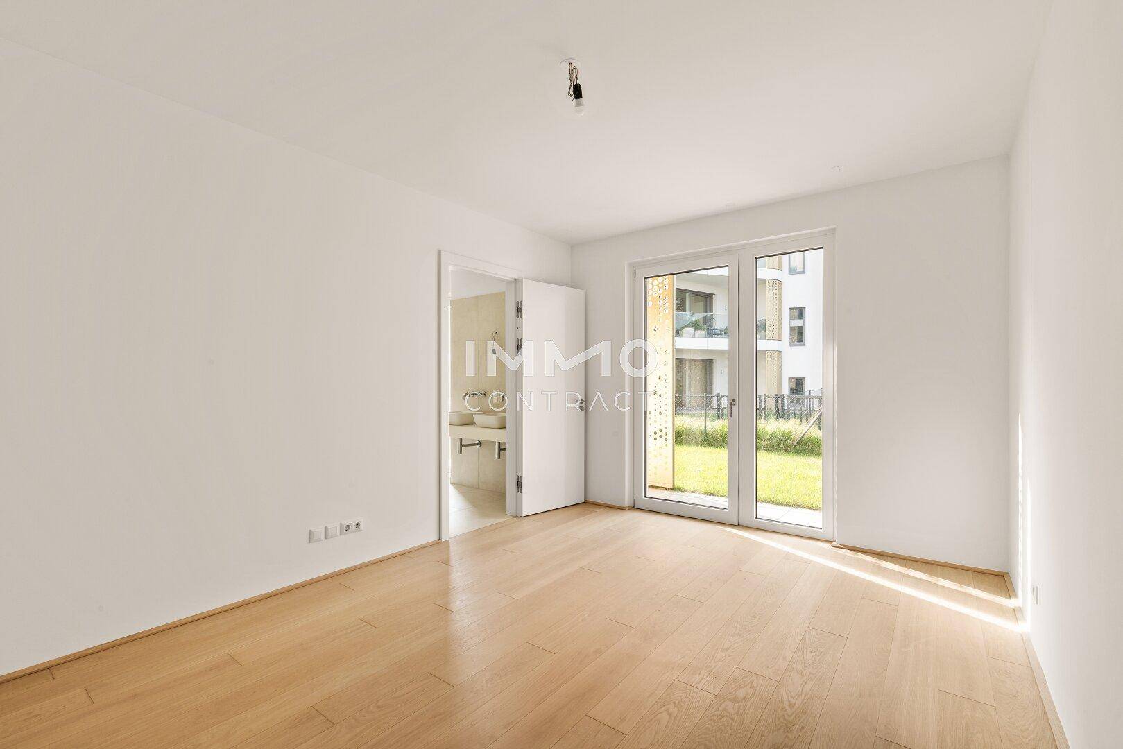 Schlafzimmer mit Holzboden, Zugang zum Garten und angrenzendem Badezimmer.