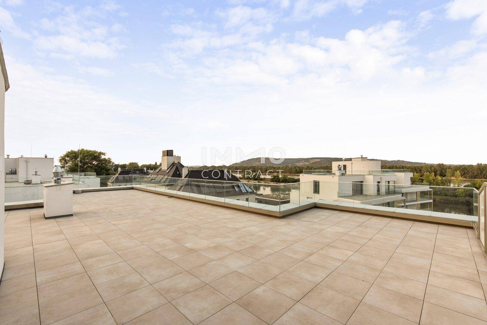 Weitläufige Dachterrasse mit Fliesenboden und Glasgeländer, bietet Panoramablick.